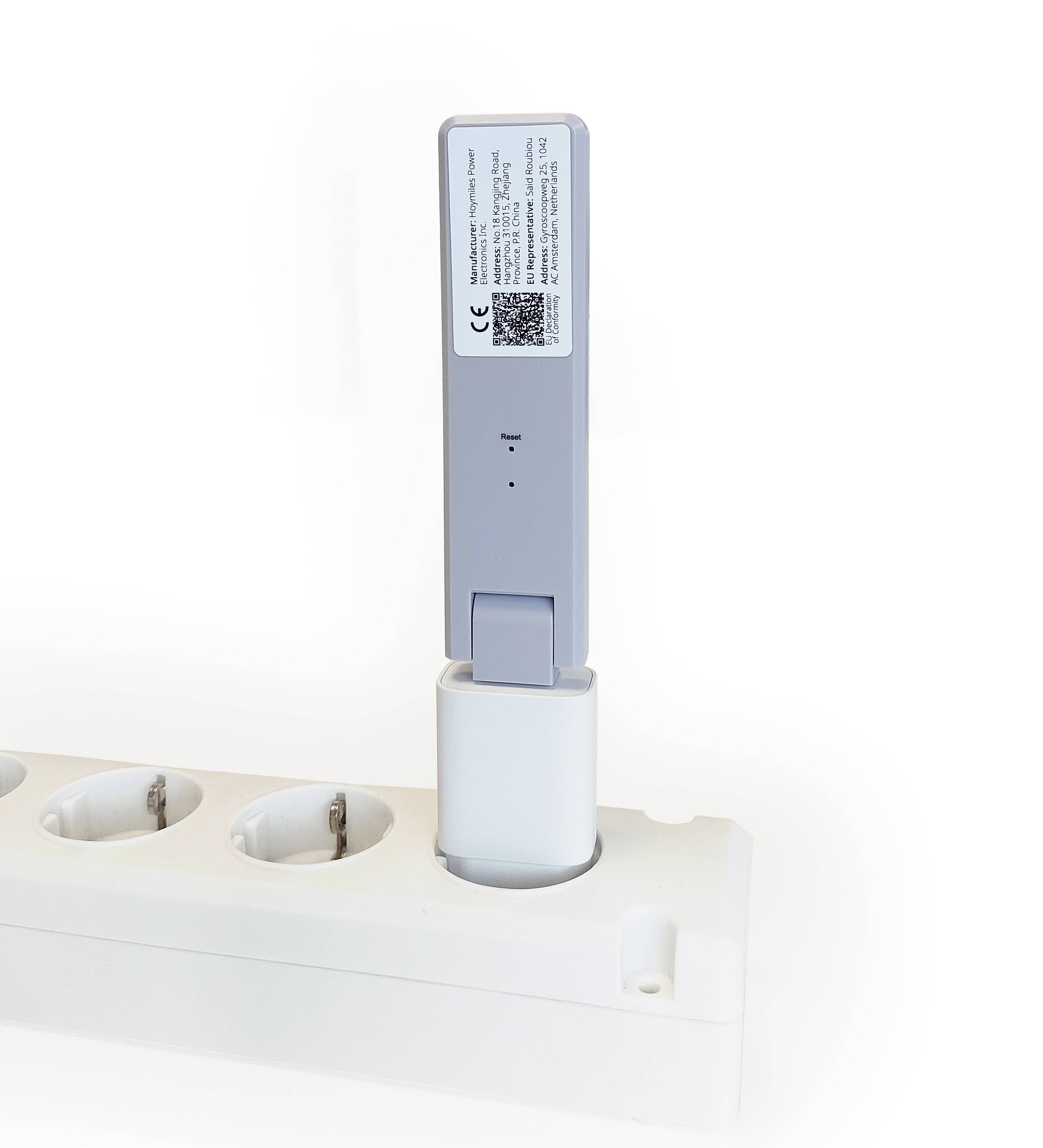 Szare urządzenie jest włożone w białą listwę zasilającą. Na urządzeniu znajduje się etykieta z małym tekstem i kodem QR.