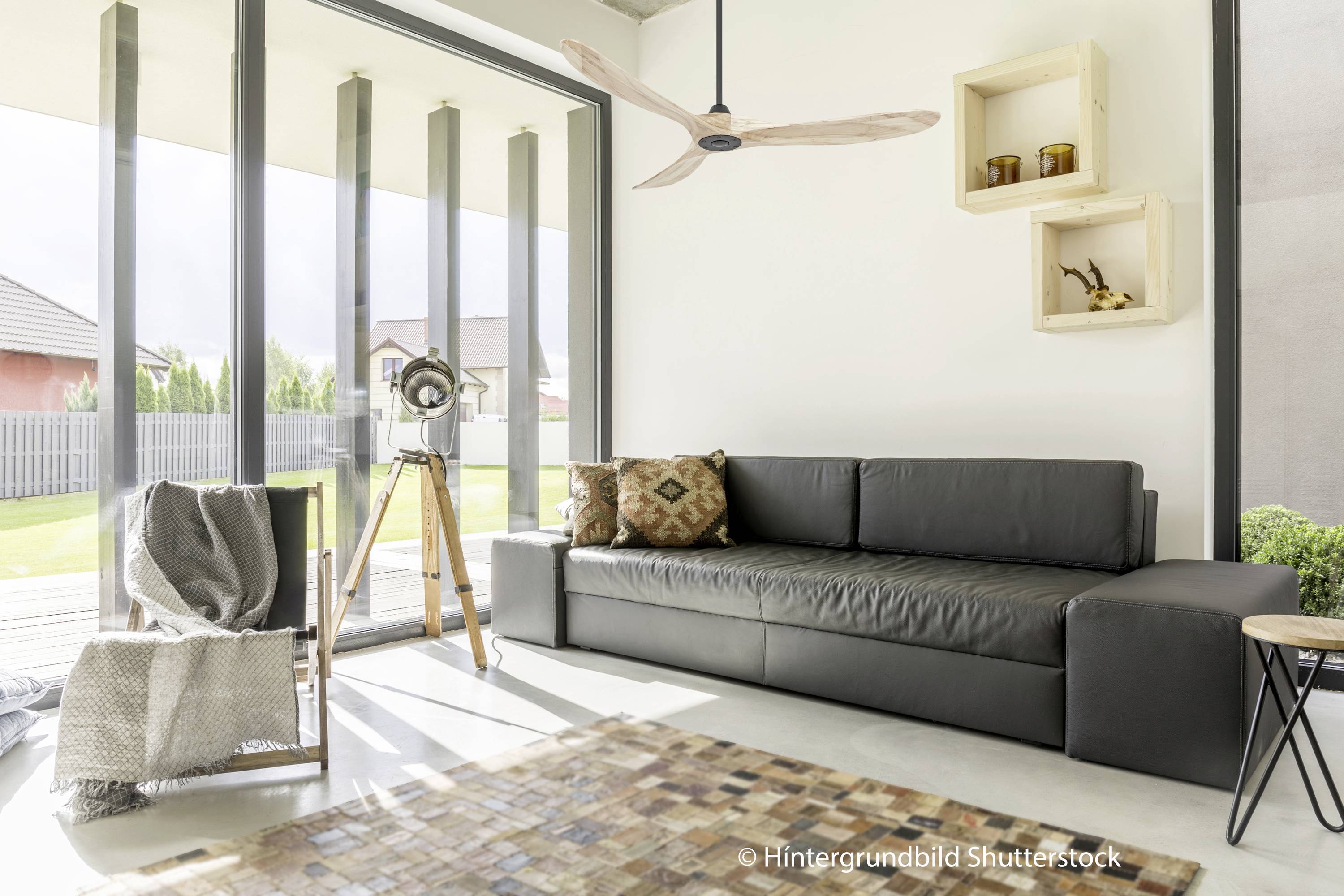 Salon z czarną skórzaną sofą, drewnianą podłogą, dużym oknem, lampą stojącą i drewnianymi regałami, które emanują nowoczesną elegancją.