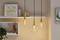 Kilka wiszących lamp świeci na ścianie nad regałem z książkami i dekoracjami. Na ścianie wisi obraz z napisem 'Myśl pozytywnie'.