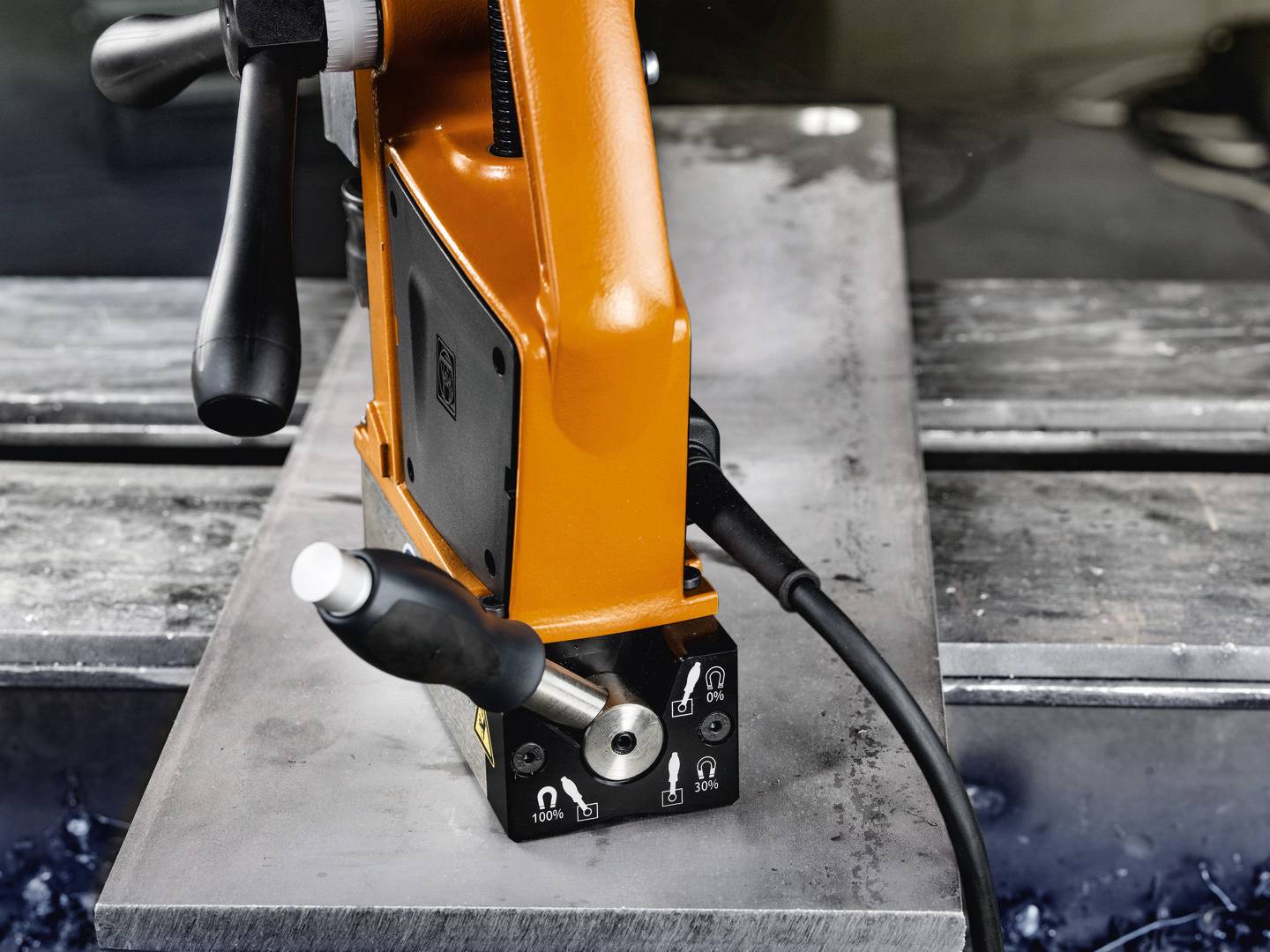 Pomarańczowe magnetyczne narzędzie wiertnicze jest umieszczone na płycie metalowej, gotowe do użycia.