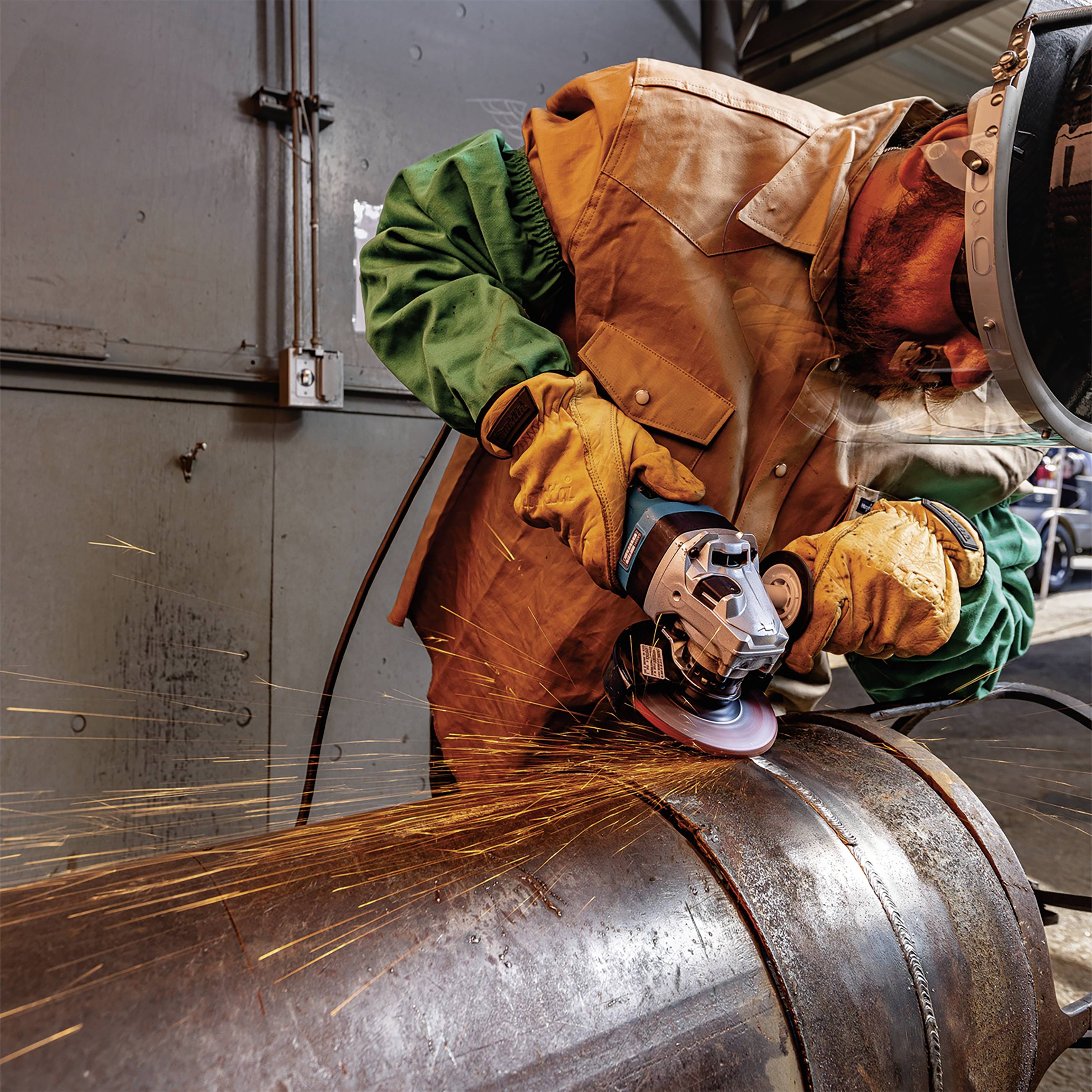 Robotnik ucina metal szlifierką kątową. Lecą iskry. Robotnik jest ubrany w odzież ochronną i okulary ochronne.