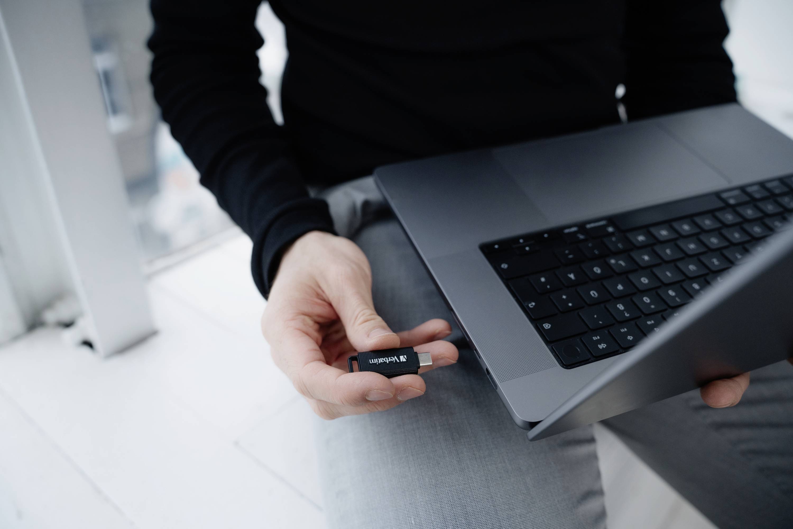 Osoba wkłada pendrive'a do laptopa stojącego na stole. Fokus jest skierowany na transfer danych.