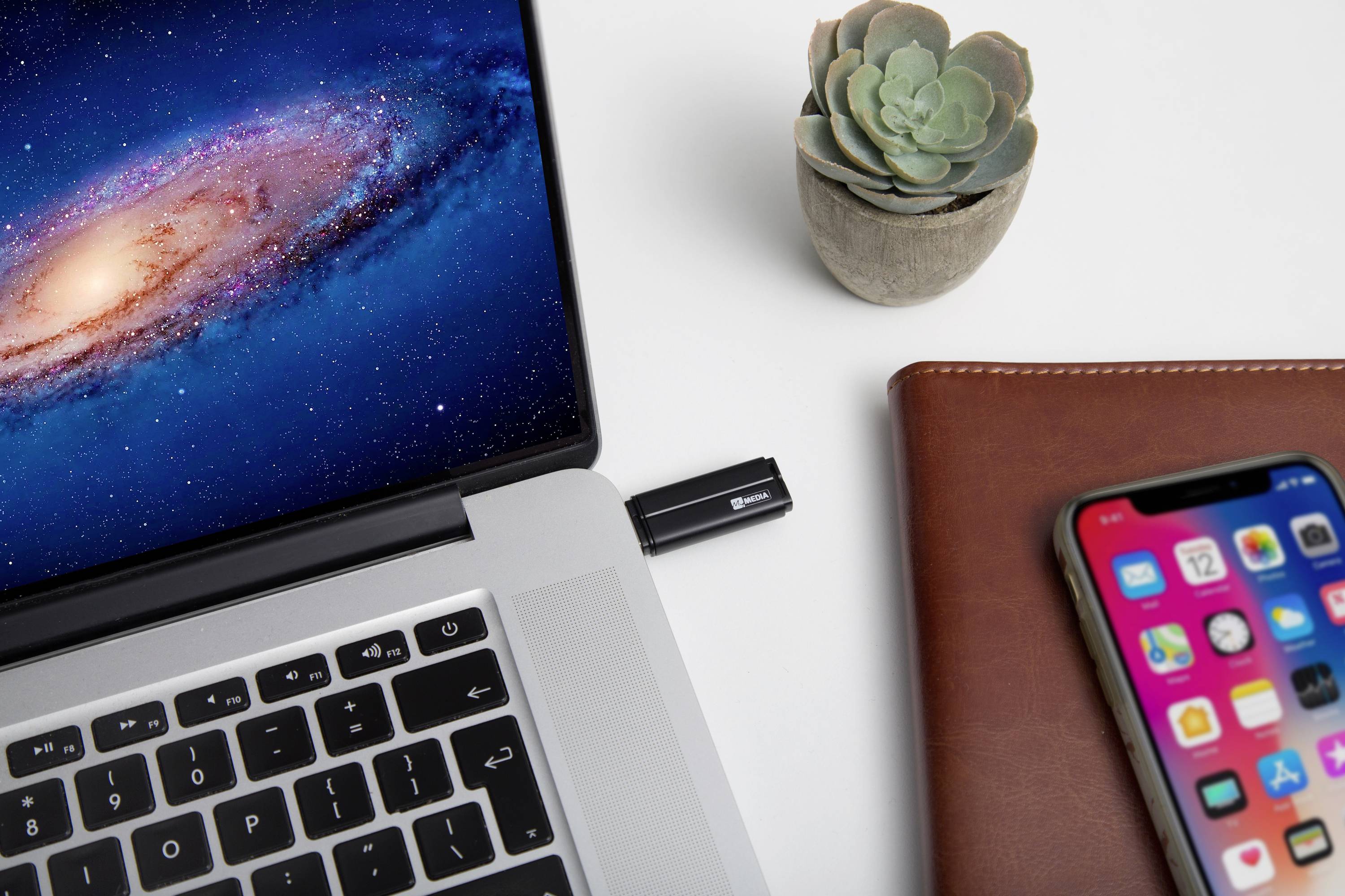 Laptop z podłączonym urządzeniem USB stoi na biurku obok smartfona, notatnika i małej sukulenty.