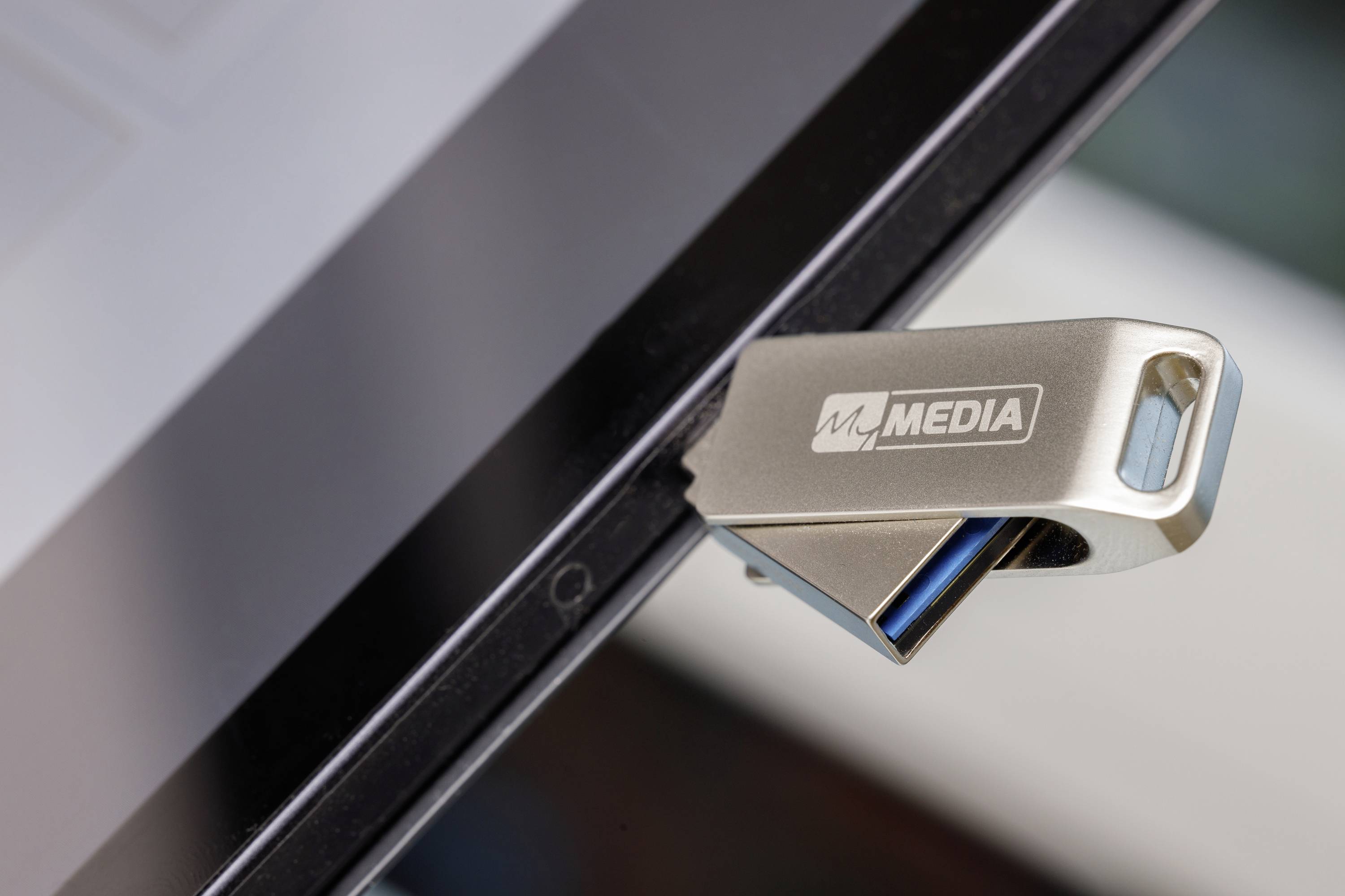 Pendrive 'MM Media' włożony jest do laptopa. Marka jest widoczna na nośniku, który został wsunięty do czarnego laptopa.