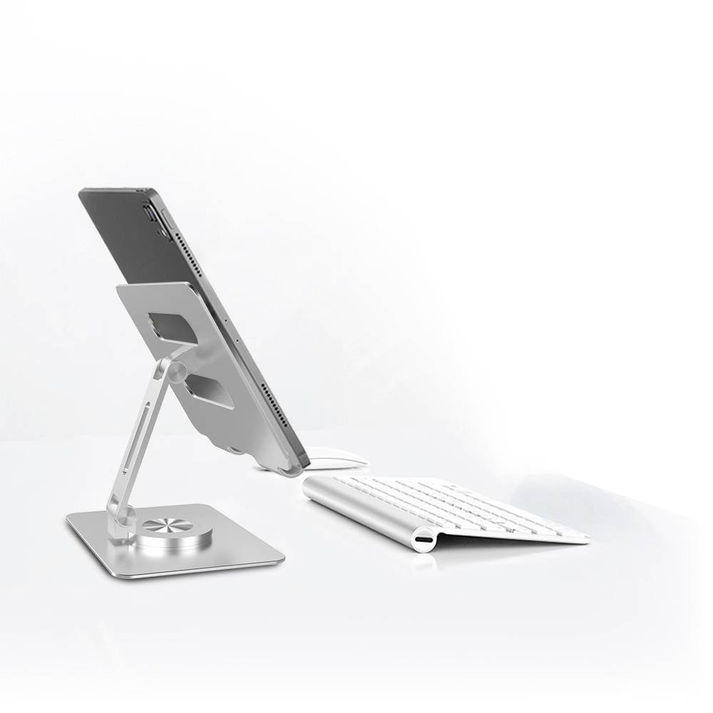 Laptop stoi na regulowanym, srebrnym stojaku obok białej, bezprzewodowej klawiatury na białym tle.