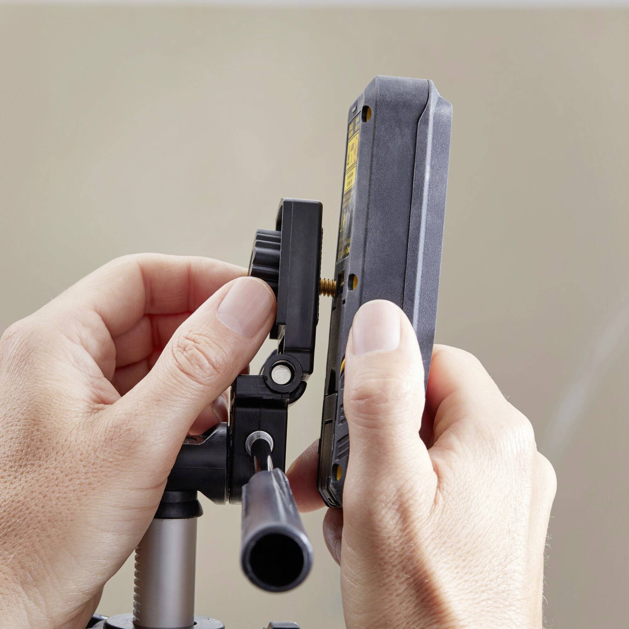 Ręce regulują przyrząd pomiarowy w statywie, który wydaje się być przeznaczony do precyzyjnych pomiarów.