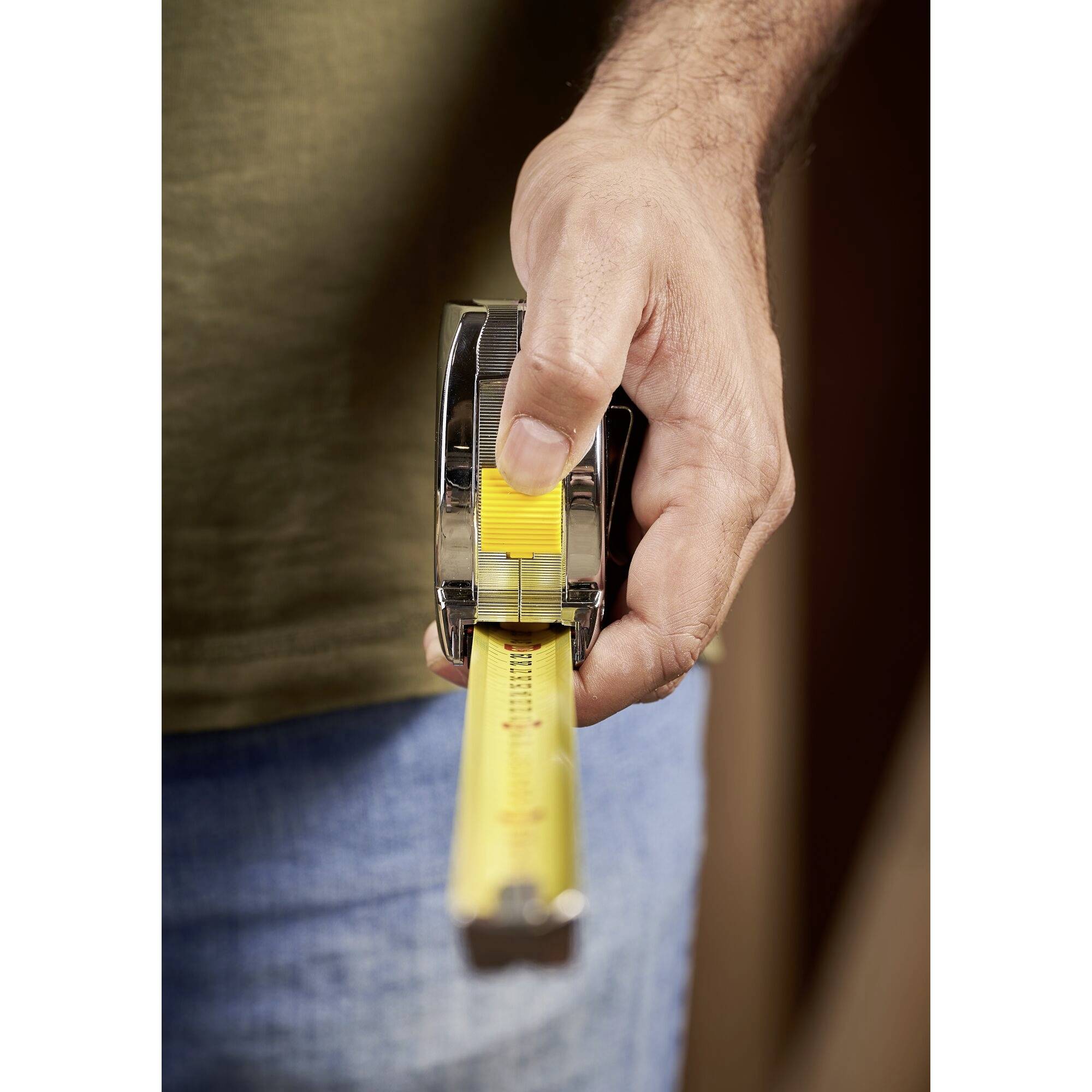 Jedna ręka trzyma miarkę rozciągniętą w kierunku widza. Podkreśla to nacisk na precyzję pomiarów.