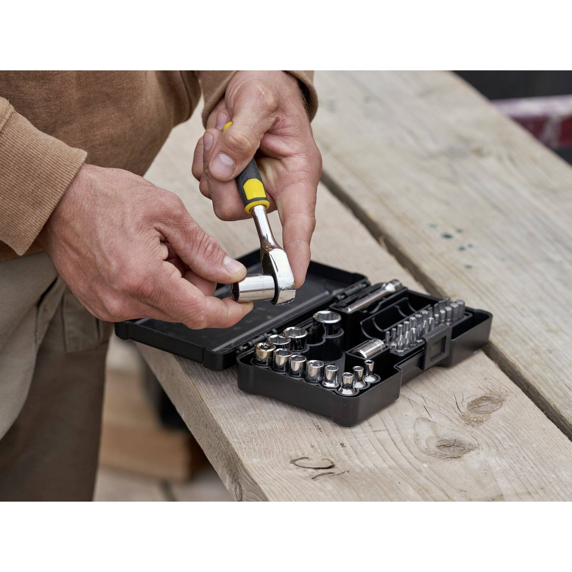 Osoba naprawia śrubę kluczem z zestawu narzędzi leżącego na drewnianym stole.