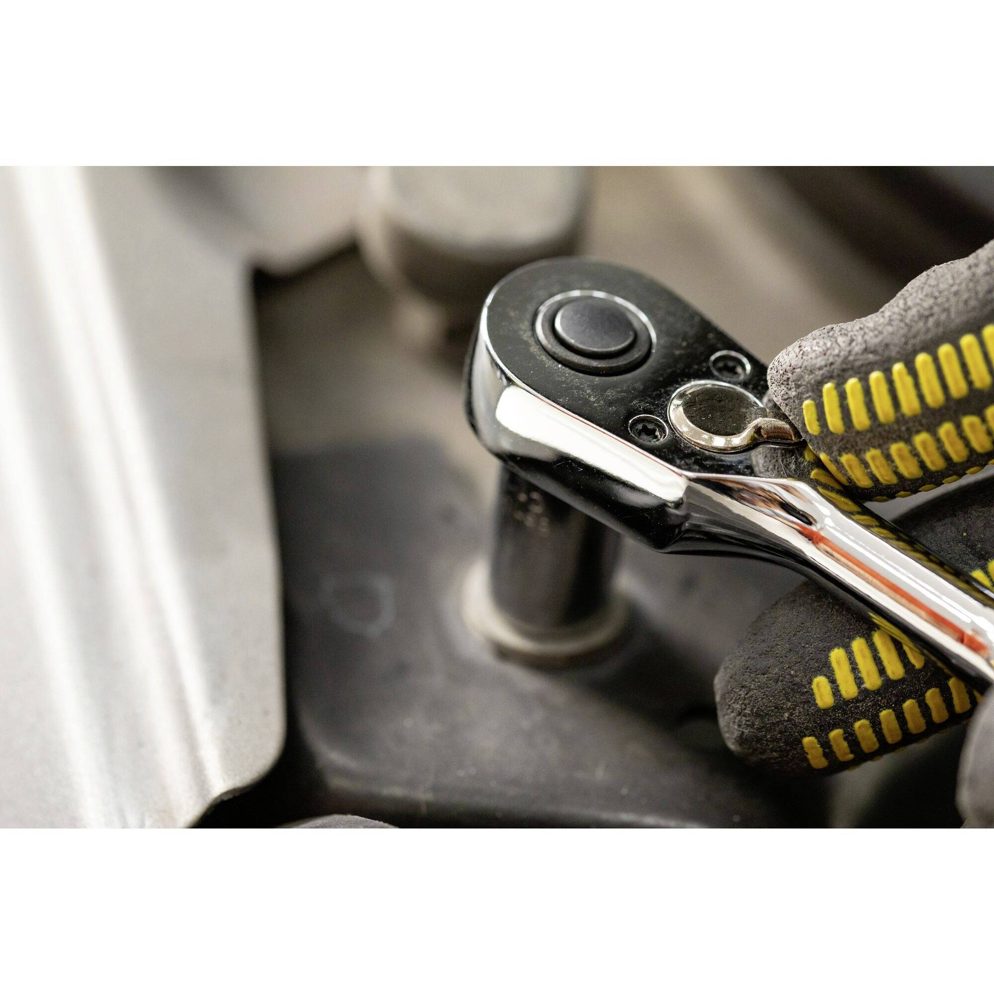 Dłoń w rękawicy trzyma klucz i majstruje przy bloku silnika. Narzędzie wygląda profesjonalnie, widać wykonywanie pracy przy maszynie.