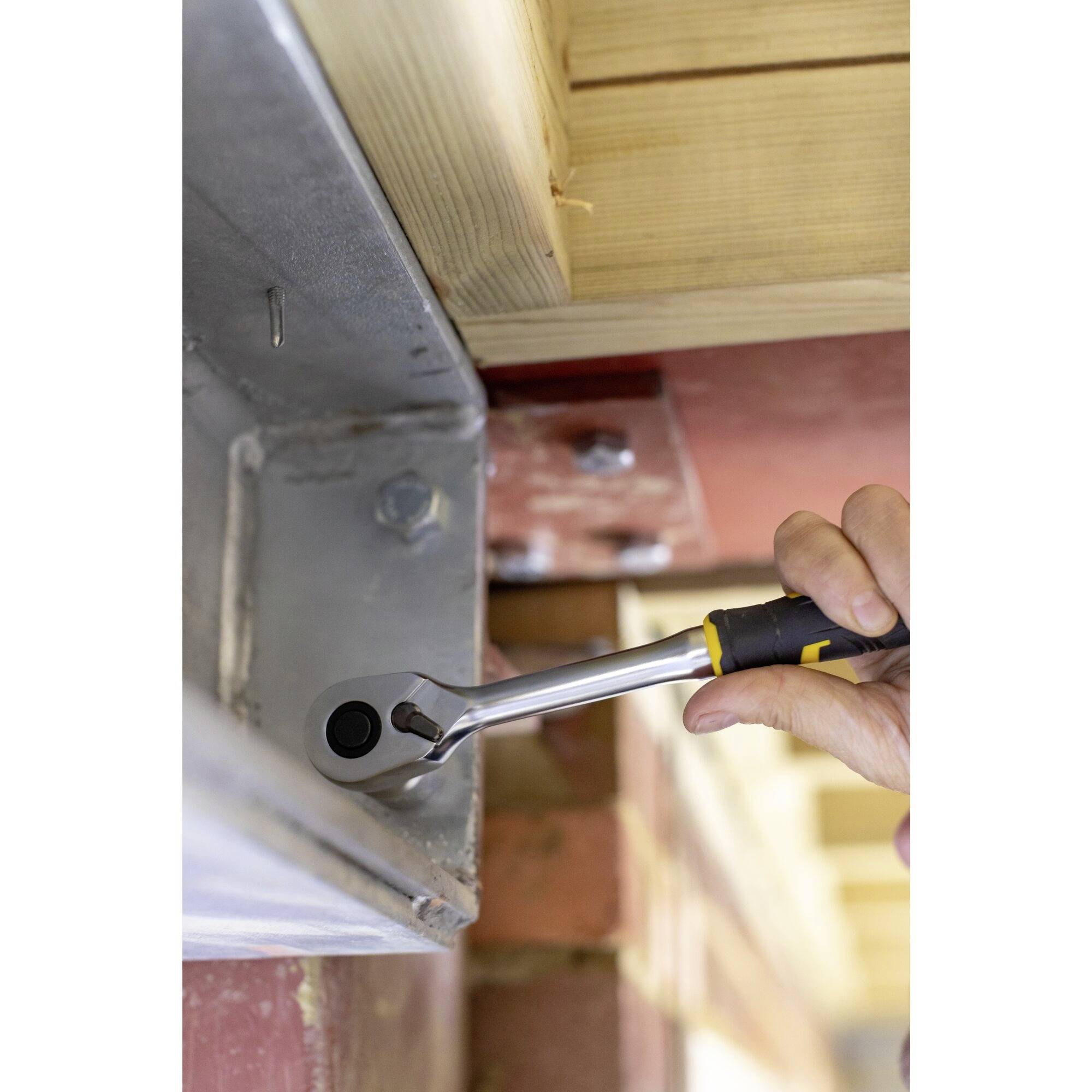 Osoba dokręca śrubę kluczem na metalowym elemencie, aby zamocować drewnianą konstrukcję.
