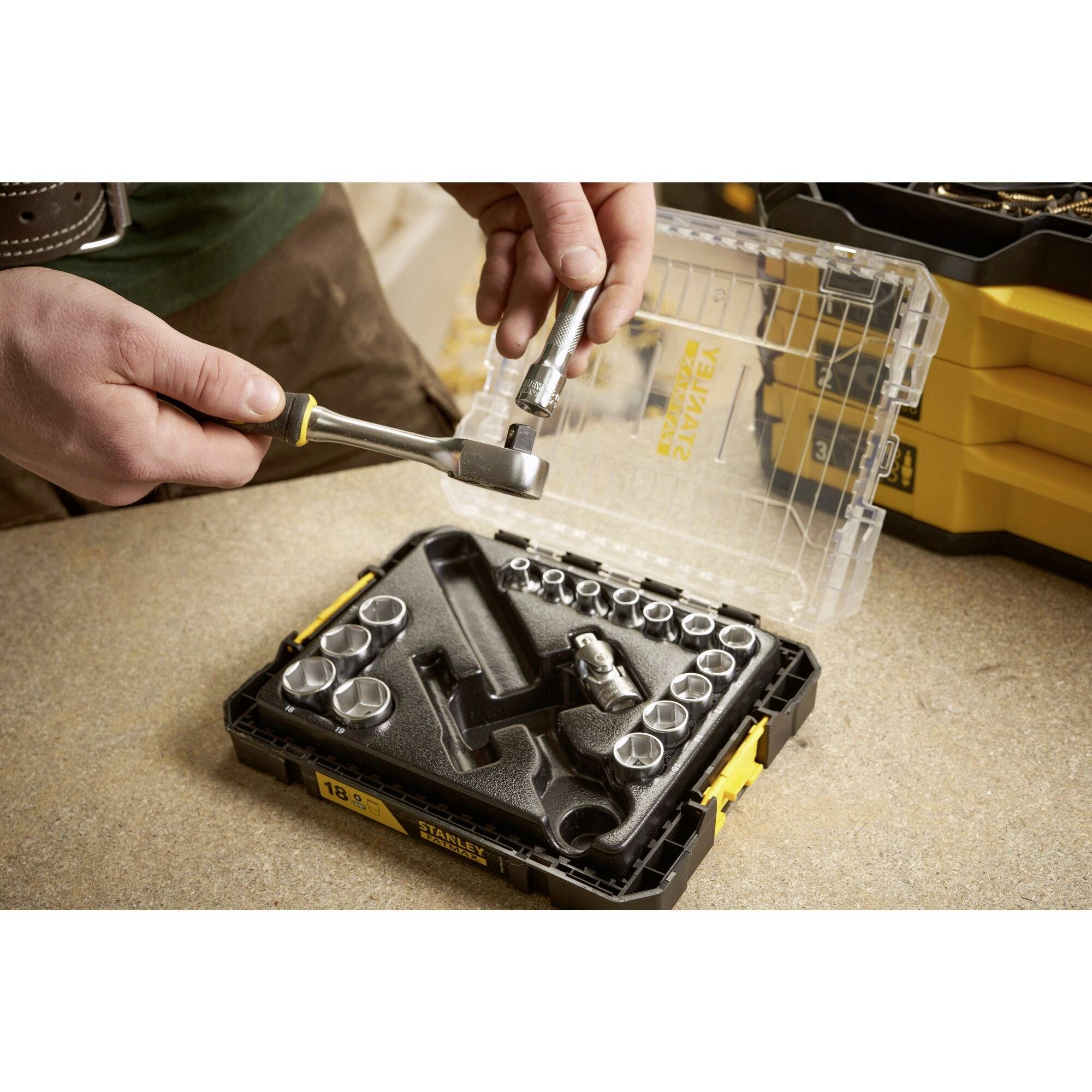 Osoba trzyma małą metalową tulejkę nad kluczem nasadowym, obok otwartej skrzynki narzędziowej z różnymi nasadkami.