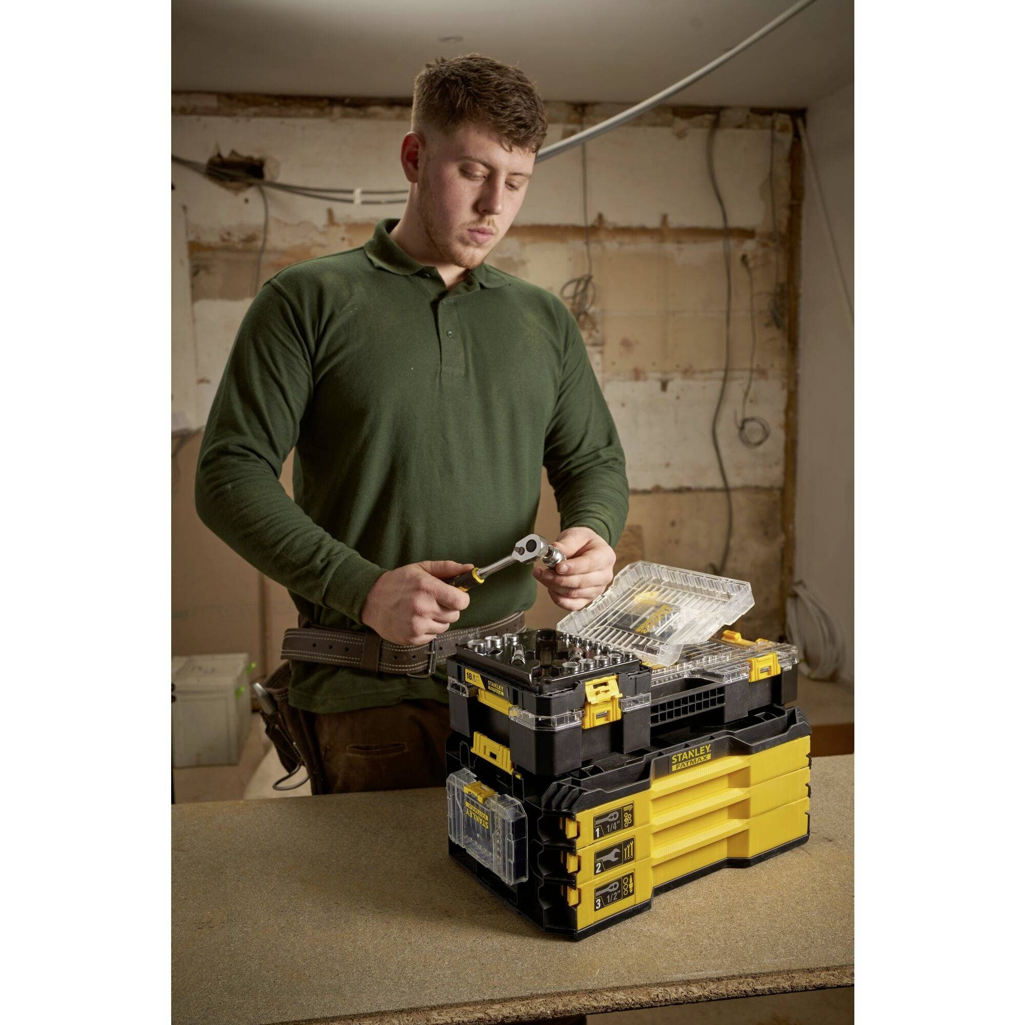 Osoba pracuje przy skrzynce narzędziowej i trzyma narzędzie na budowie lub w warsztacie.