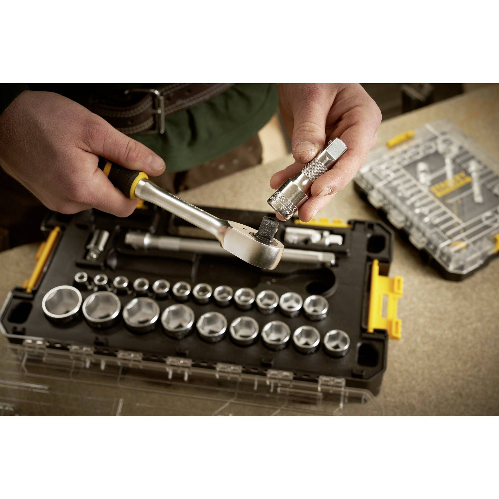 Zestaw kluczy nasadowych z różnymi końcówkami jest trzymany przez jedną osobę, gotowy do użycia na stole warsztatowym.