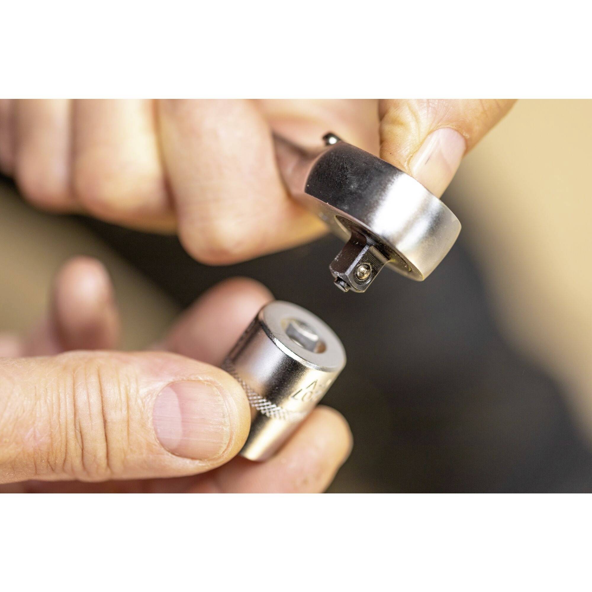 Dłoń łączy klucz nasadowy z mechanizmem grzechotki. Fokus skierowany jest na zatrzaśnięcie elementów, aby utworzyć stabilne połączenie.