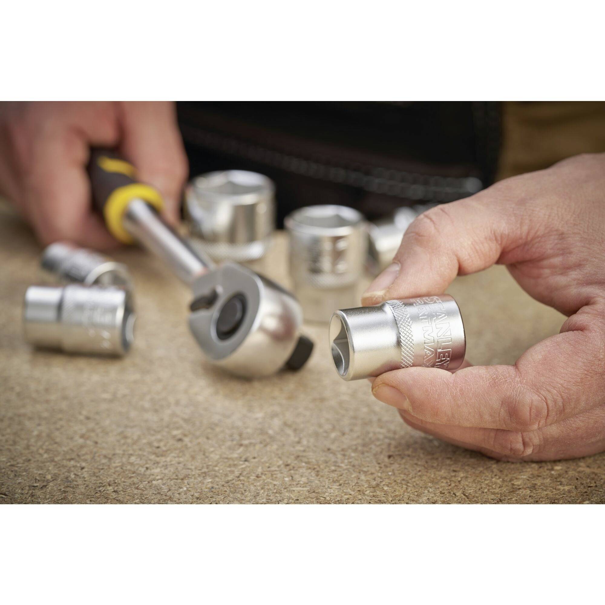 Kilka kluczy nasadowych i klucz z grzechotką leżą na stole. Ręka trzyma jeden z kluczy nasadowych.