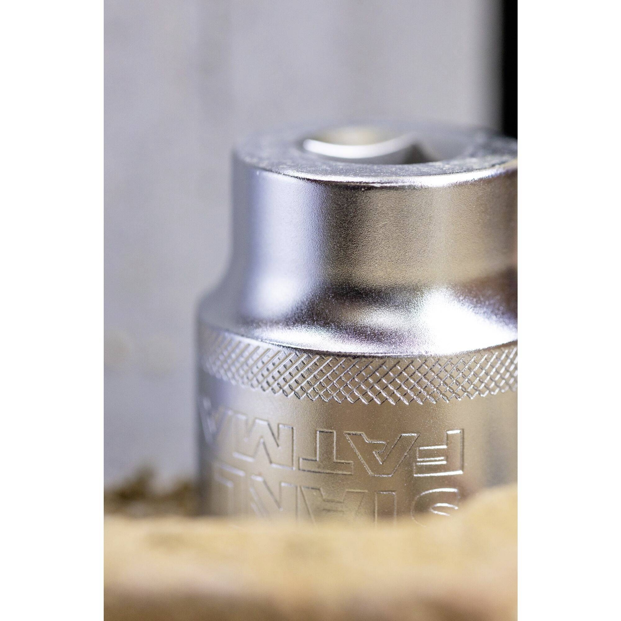 Srebrny cylinder metalowy z napisem 'Fatma' leży na rozmytym, beżowym tle.