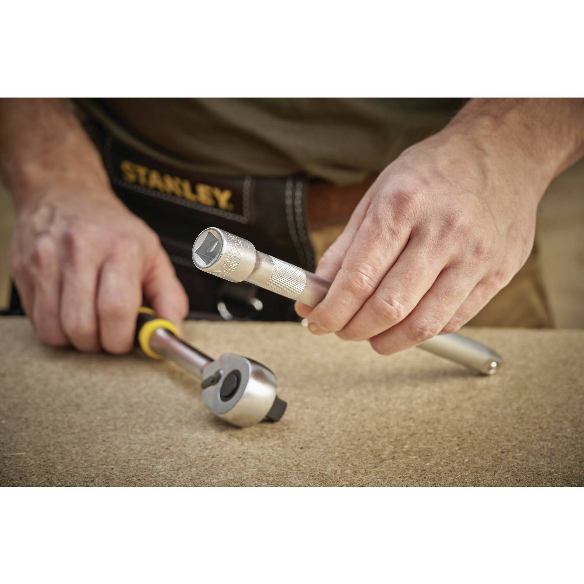 Osoba naprawia sworzeń kluczem nasadowym na warsztacie. Klucze płaskie i nasadki są widoczne.