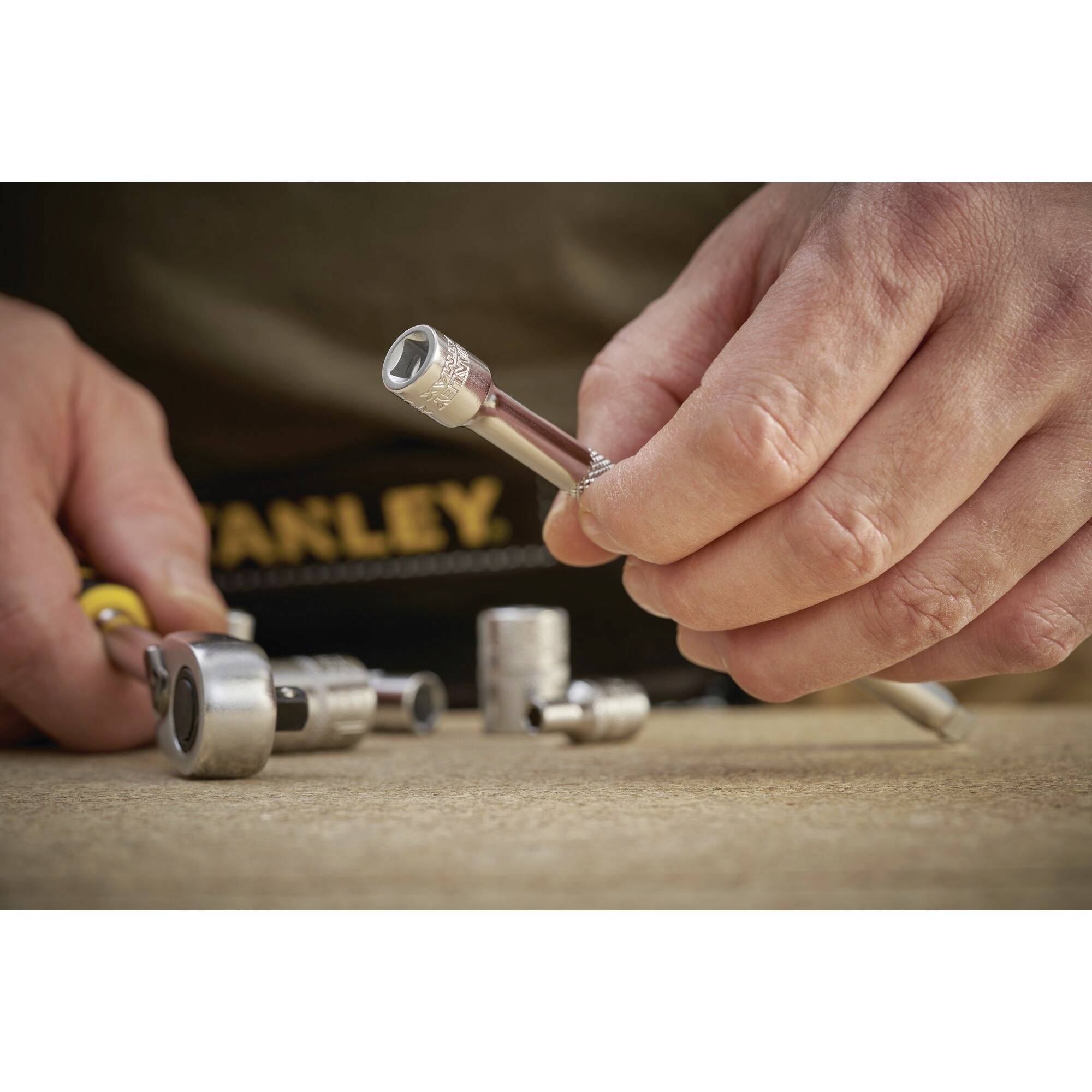 Osoba trzyma klucz nasadowy w ręku, podczas gdy na stole rozmieszcza pozostałe narzędzia. Fokus czynności skierowany jest na prace naprawcze.