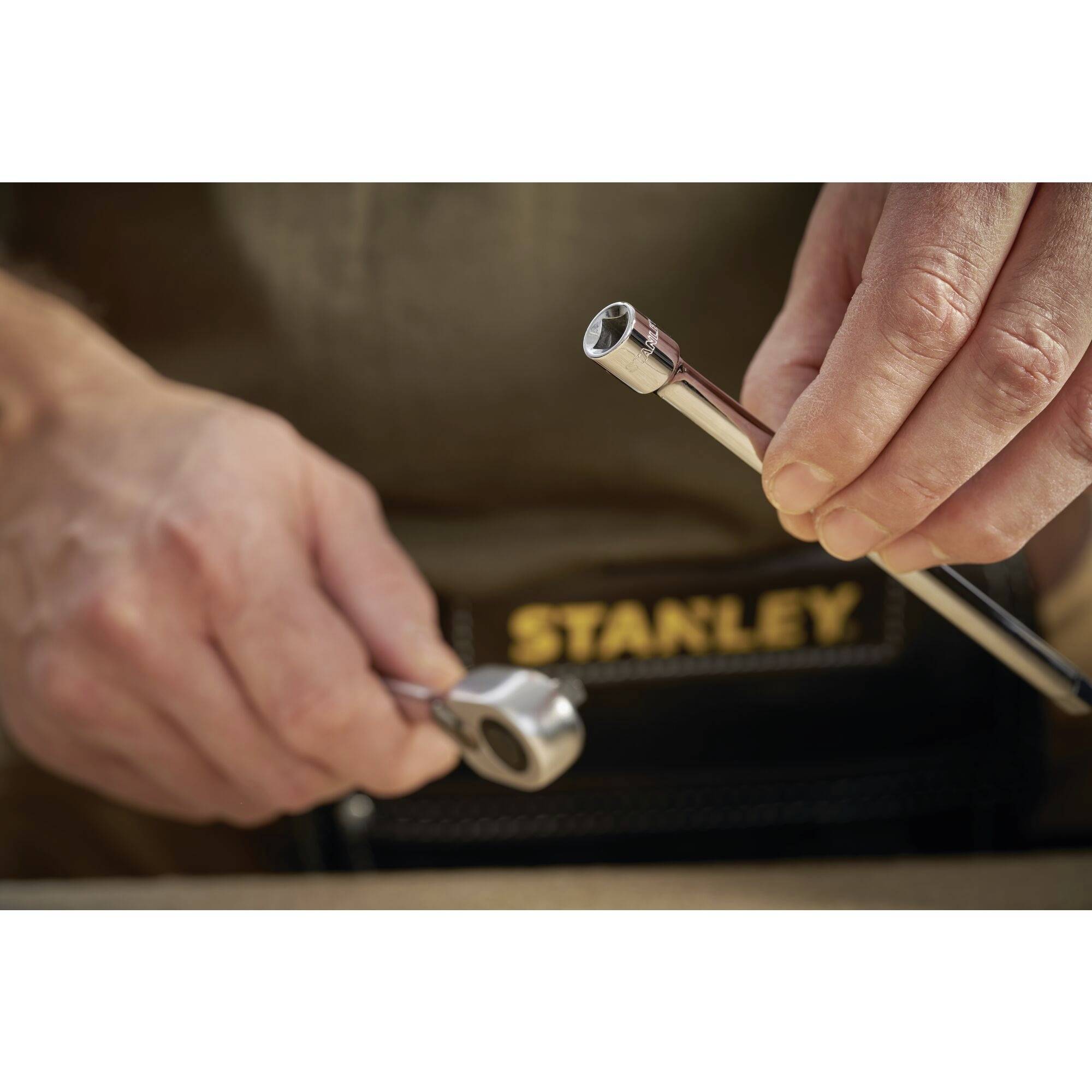 Osoba trzyma grzechotkę i klucz nasadowy z płaszczyzną klucza. Fokus na użyciu narzędzia, napis Stanley.