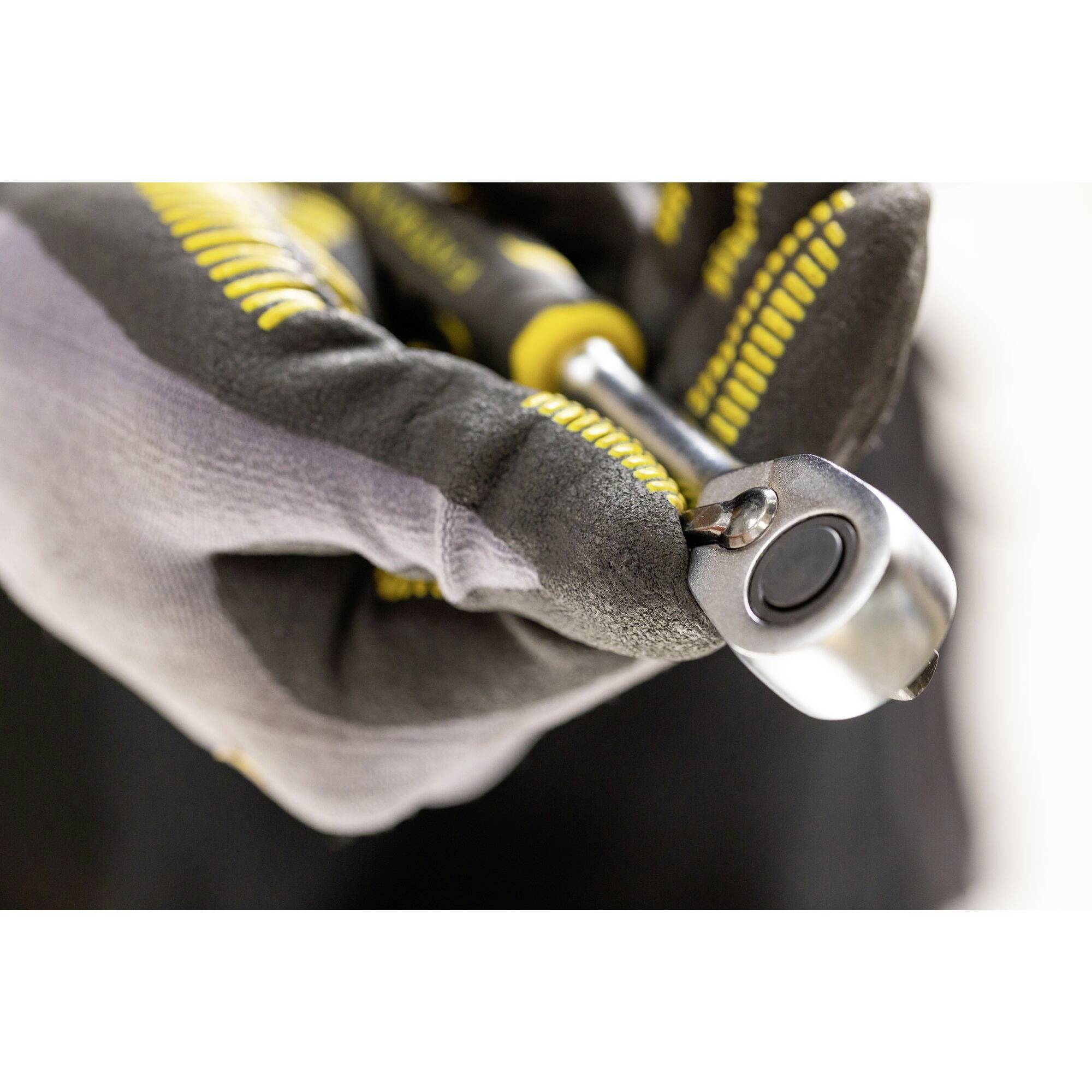 Dłoń trzymająca klucz nastawny z żółtą rękojeścią. Zbliżenie na końcówkę narzędzia, na dłoni założona jest rękawica.