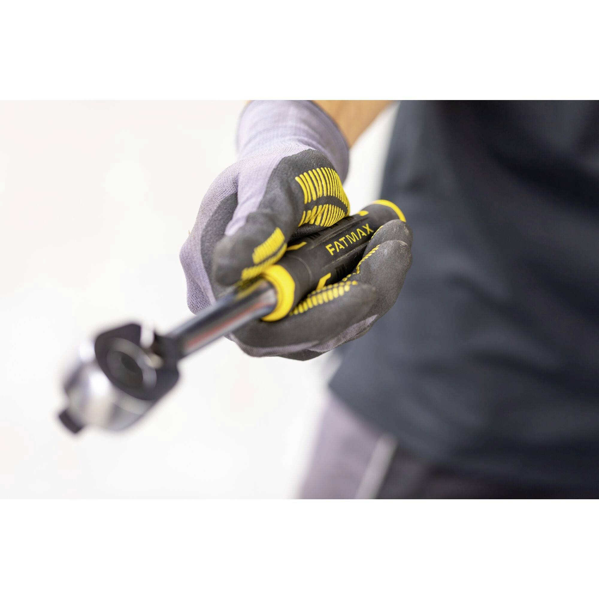 Osoba trzyma narzędzie z żółto-czarnym uchwytem, jednocześnie nosząc rękawice robocze.