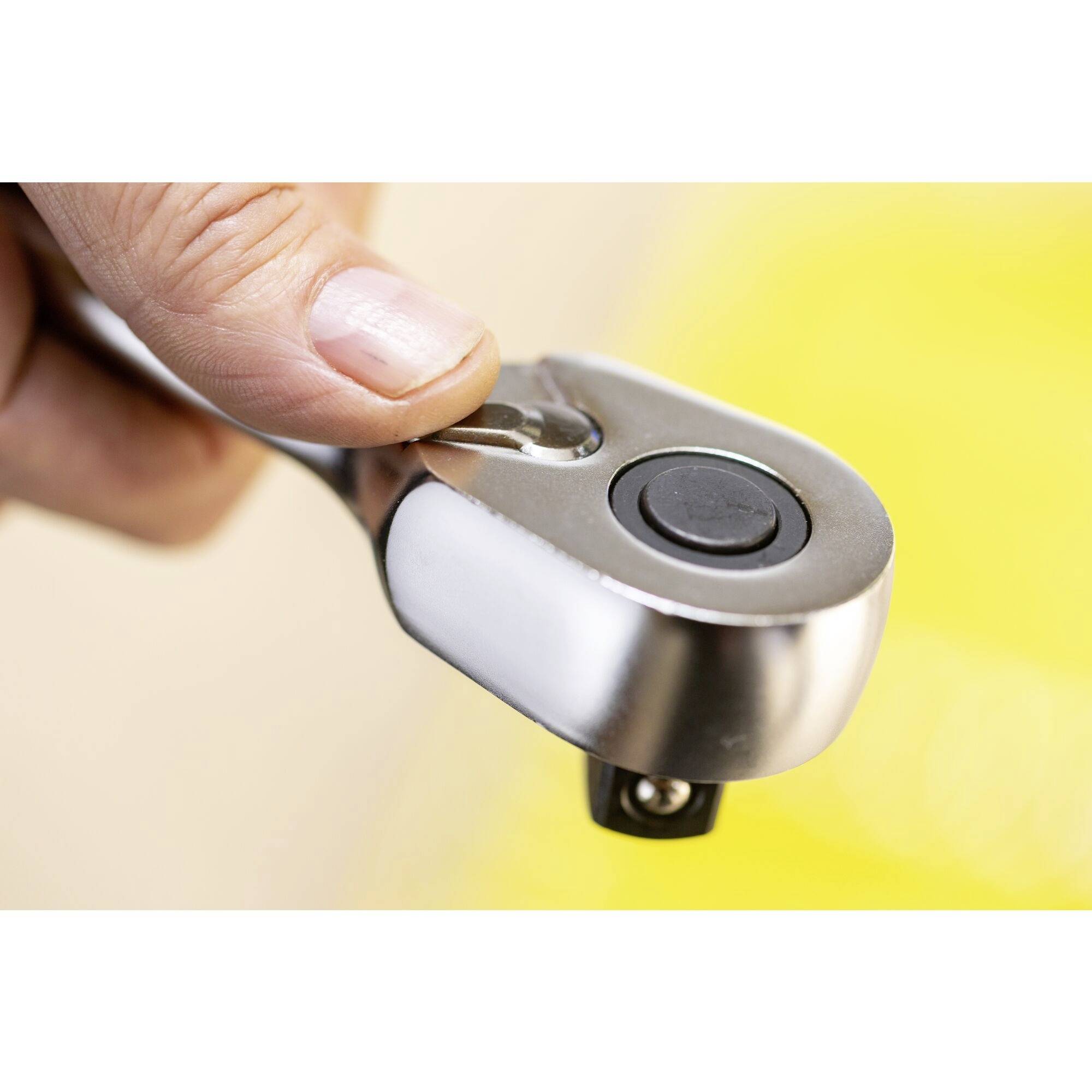 Jedna ręka trzyma chromowany klucz zapadkowy, gotowa do obrotu. Na tle widoczny jest rozmyty, żółty obszar.
