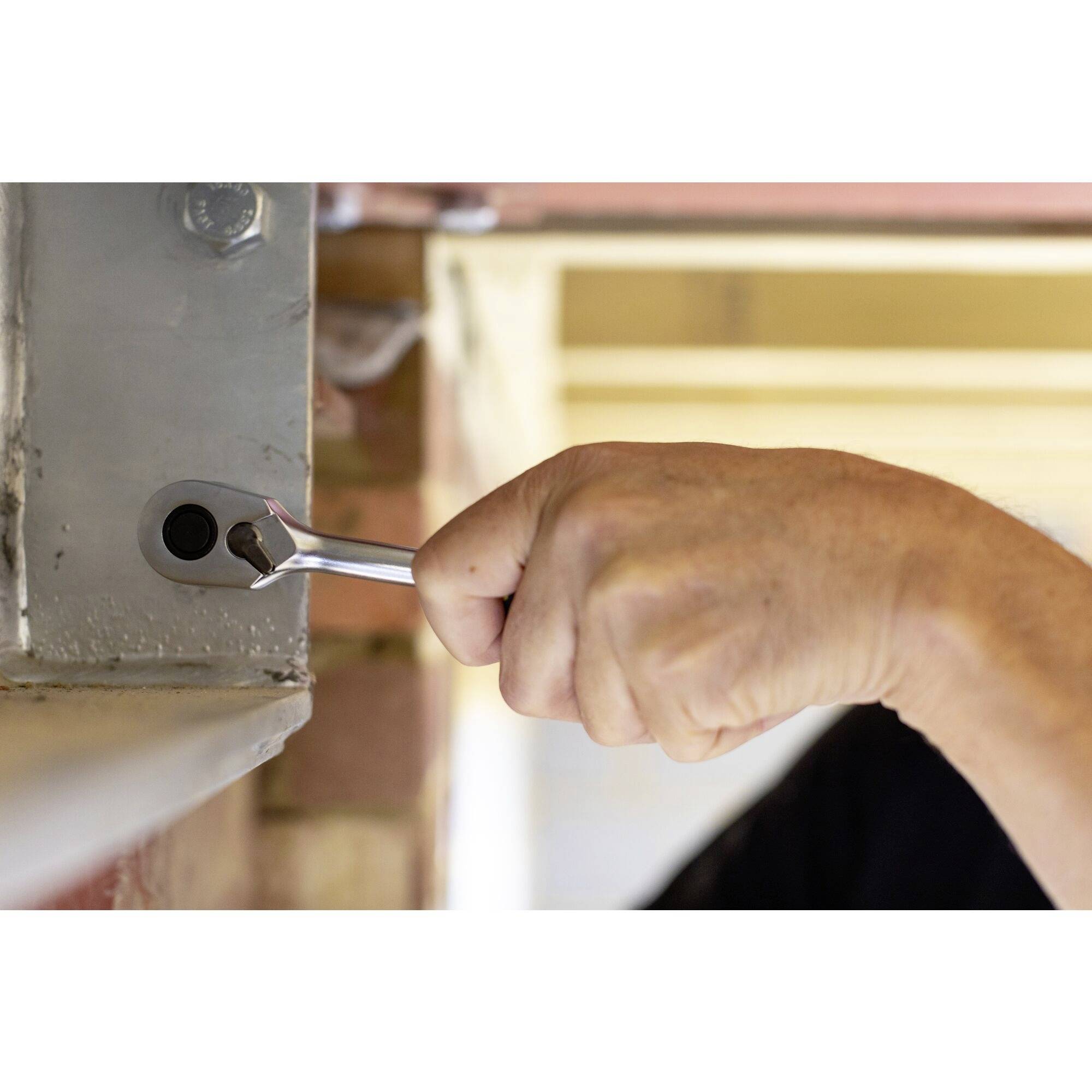 Dłoń obraca kluczem hydraulicznym, aby przymocować śrubę do metalowej ramy przy ceglastej ścianie.