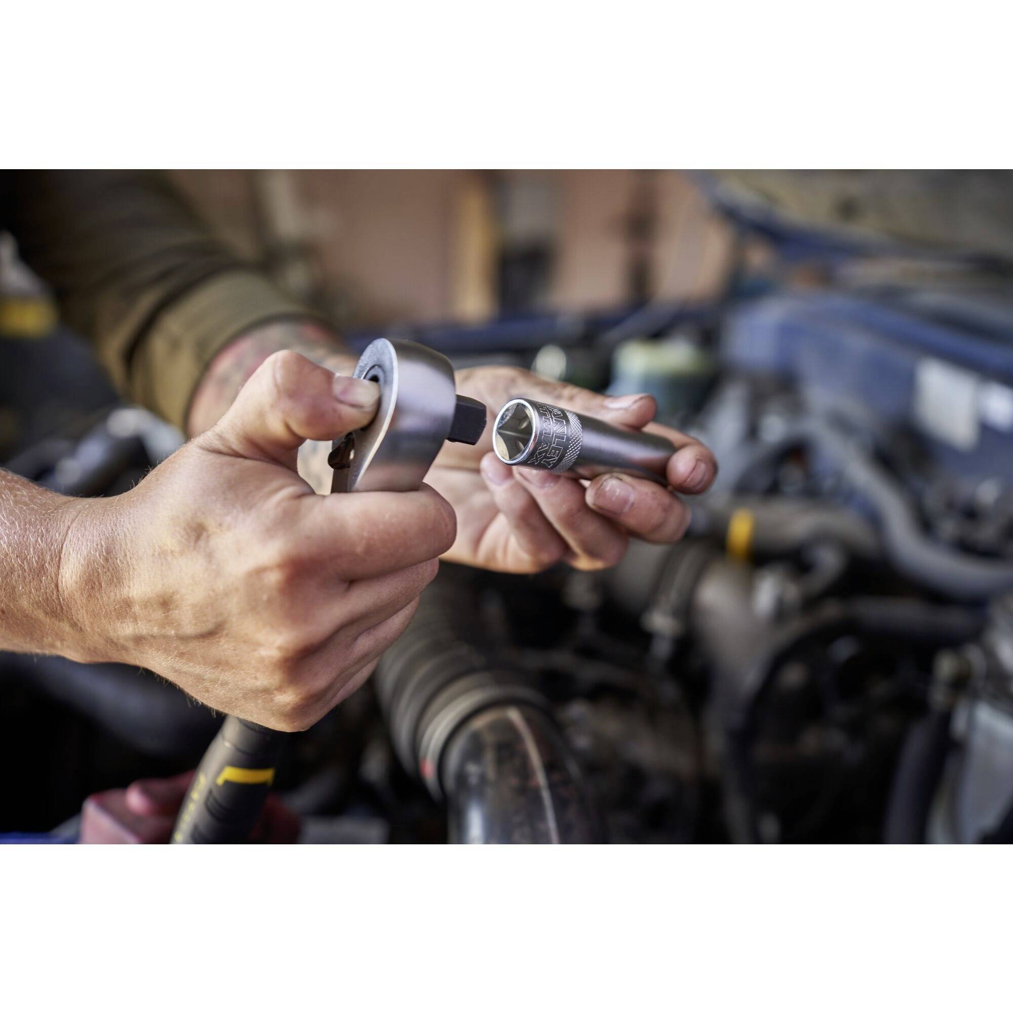 Osoba używa klucza zapadkowego do pracy przy silniku pojazdu. Dłonie w rękawicach chwytają nakrętkę narzędziową.