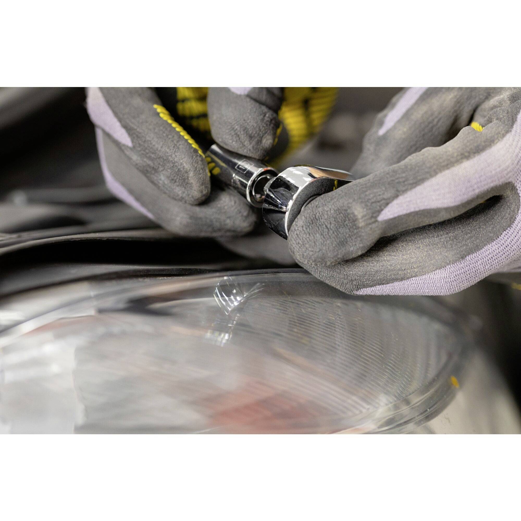 Osoba w szarych rękawiczkach wymienia żarówkę w reflektorze samochodu.