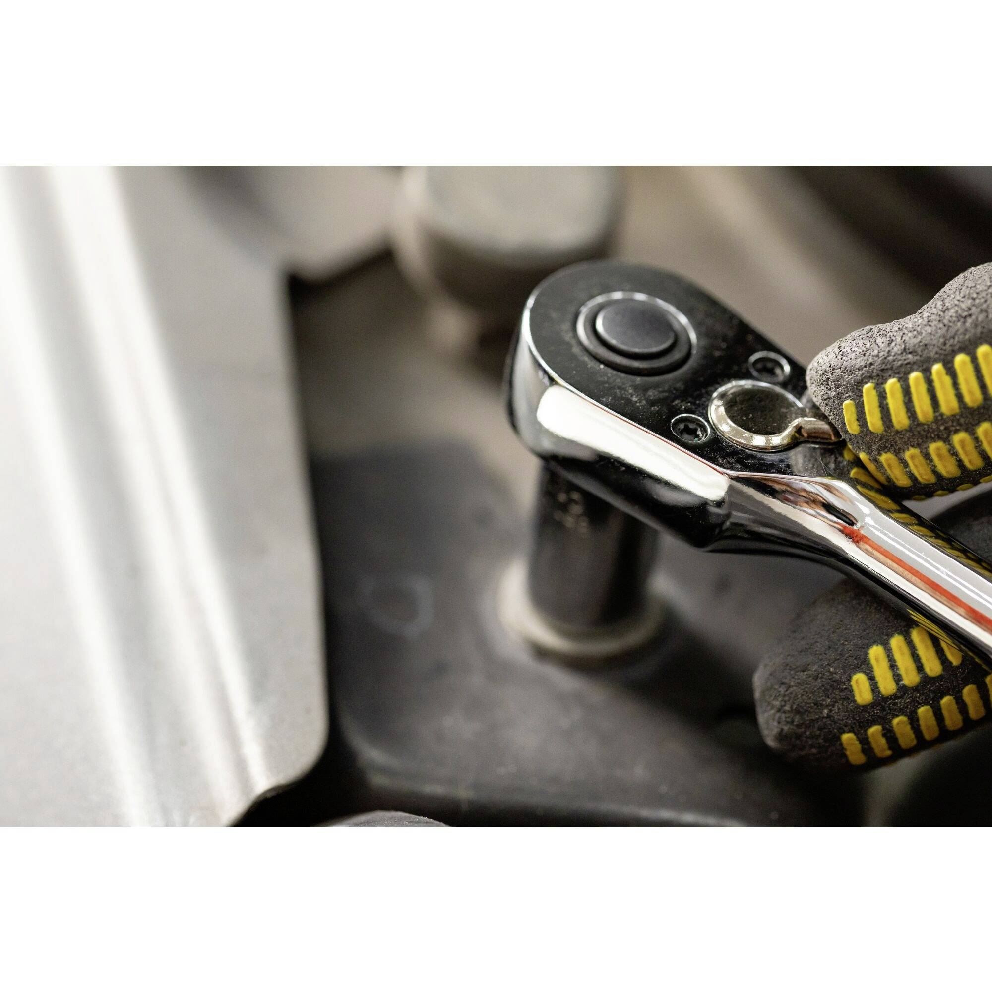 Dłoń w rękawicy trzyma srebrny klucz francuski przykładany do nakrętki. Fokus na użyciu narzędzia.