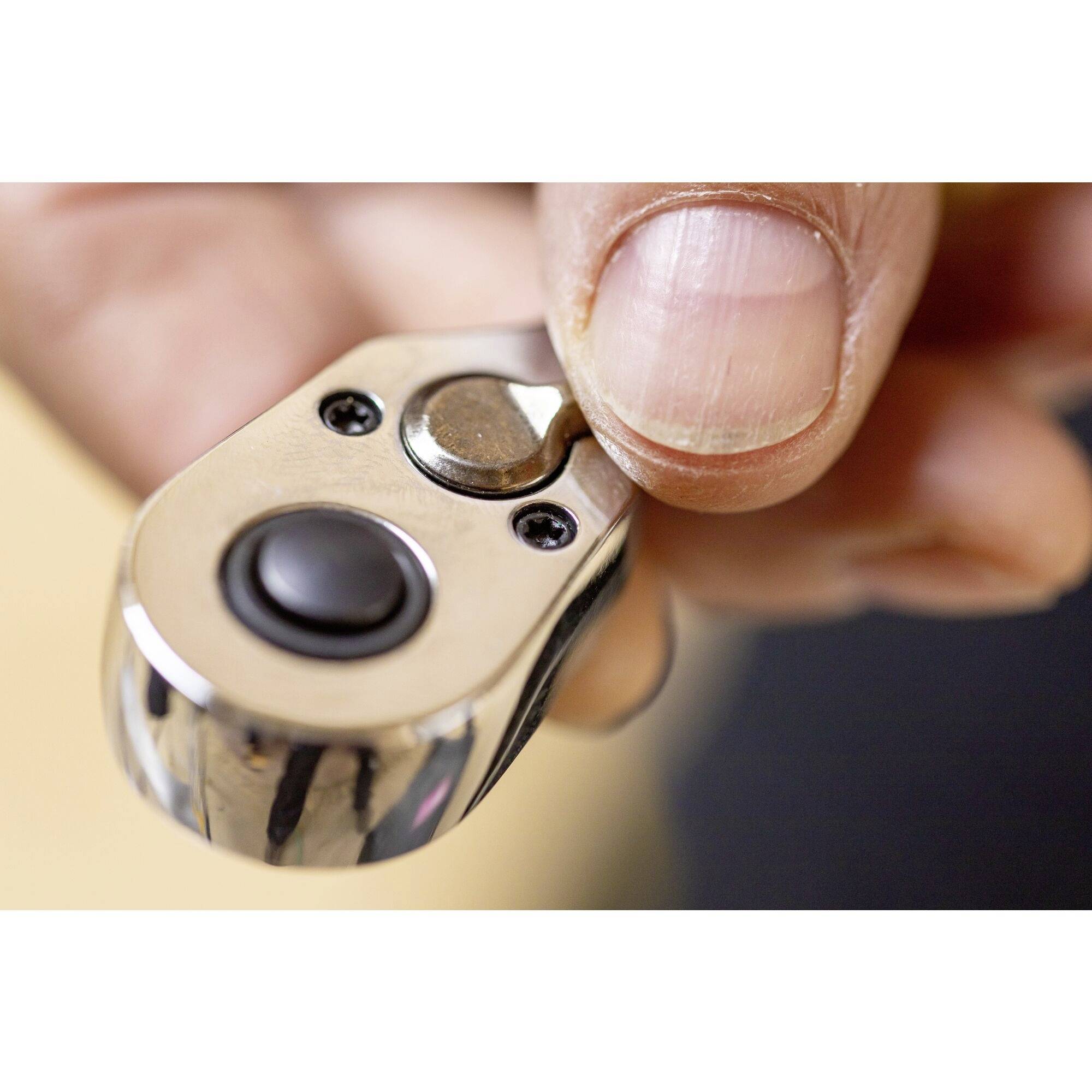 Jedna dłoń trzyma srebrną metalową zapalniczkę z czarnym przyciskiem i małym guziczkiem na pokrywie. Kciuk jest tuż nad przyciskiem zapalającym.