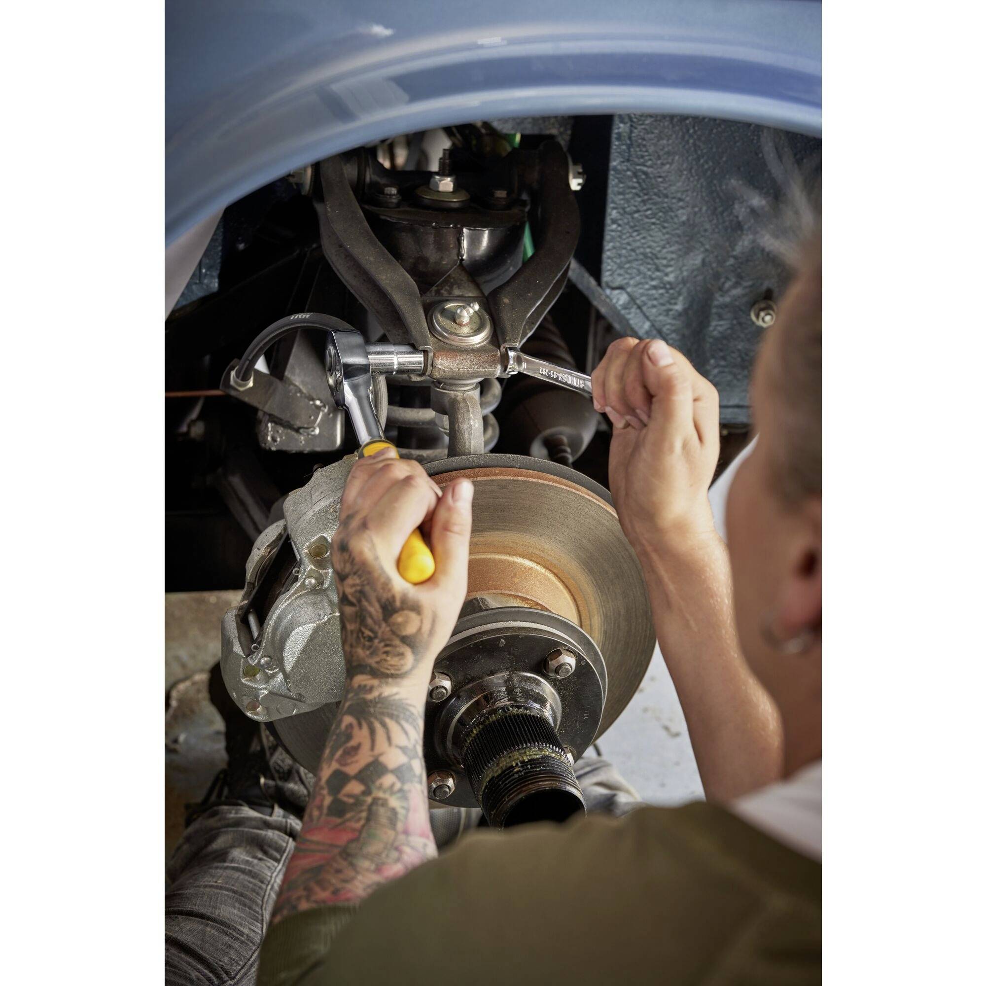 Osoba montuje układ hamulcowy w pojeździe; ręce trzymają narzędzia. Zbliżenie ukazuje technikę i koncentrację.