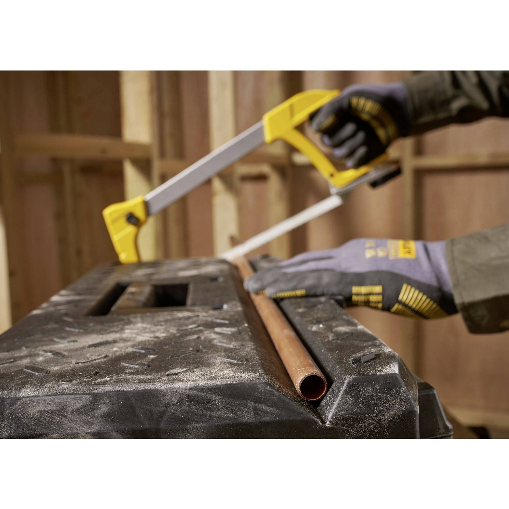 Osoba przecina rurę miedzianą ręczną piłą na stole warsztatowym. Osoba jest w rękawicach.