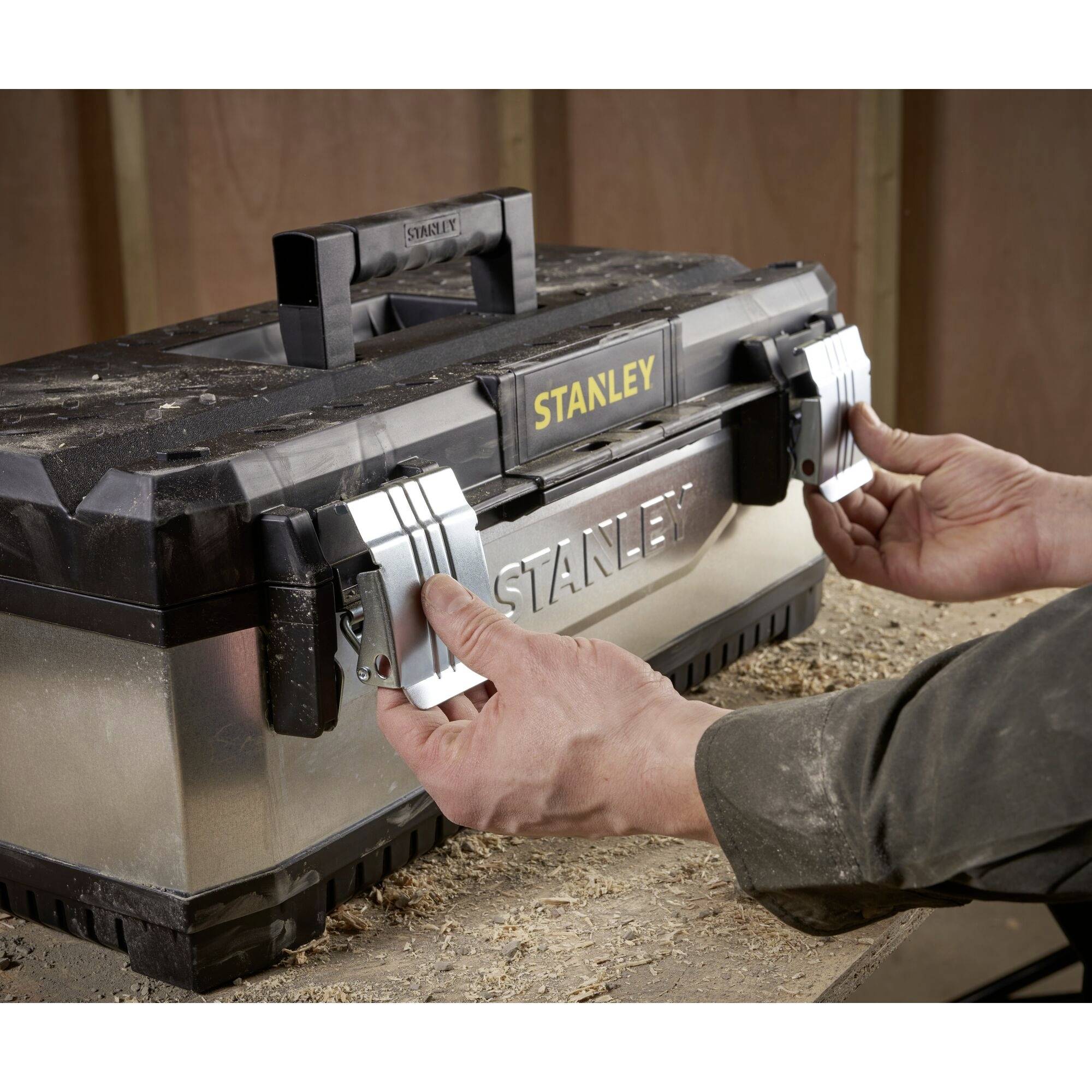 Osoba otwiera skrzynkę narzędziową Stanley w środowisku warsztatu.