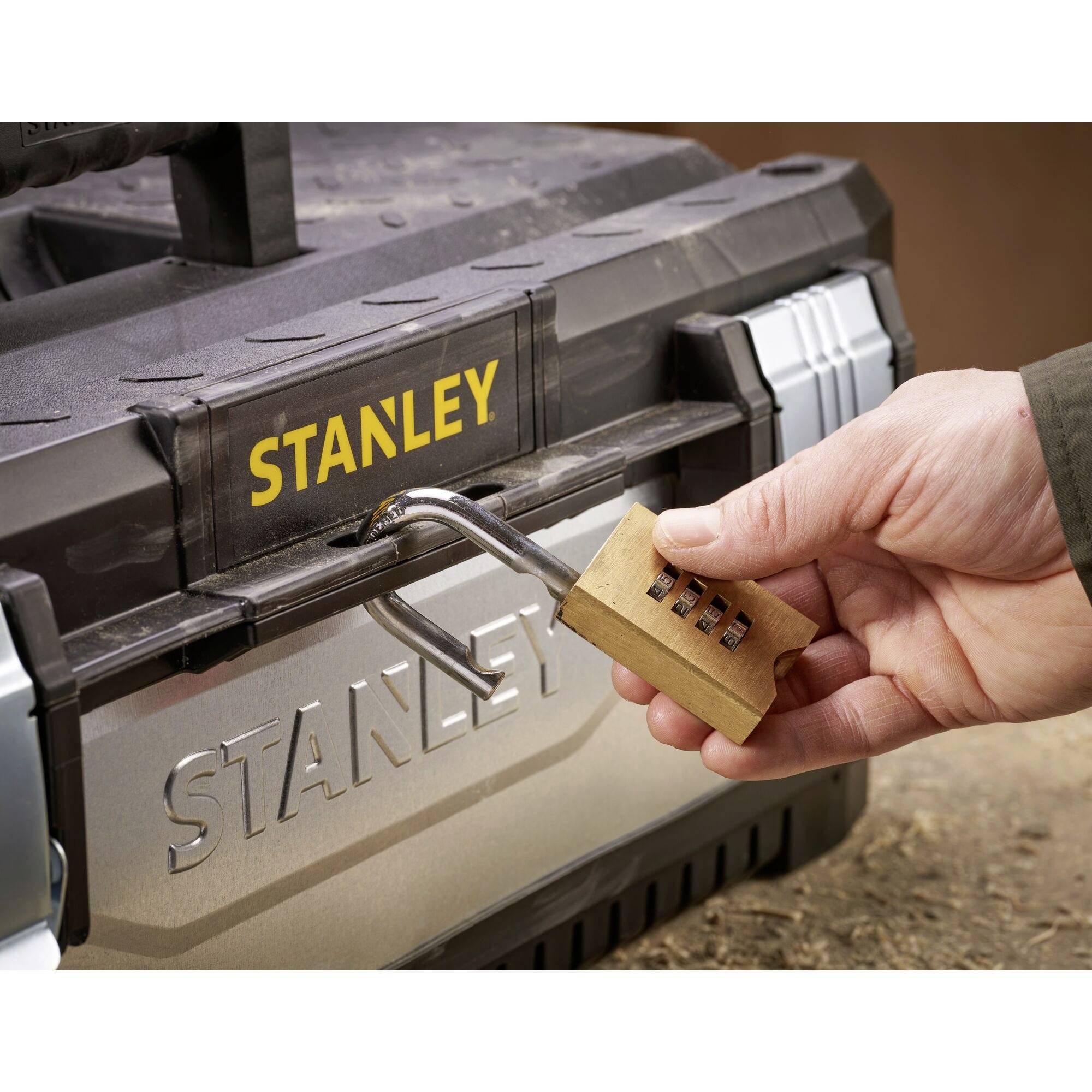 Ręka otwiera zamek szyfrowy na skrzynce narzędziowej firmy Stanley. Fokus jest skierowany na zabezpieczenie za pomocą tego zamka.