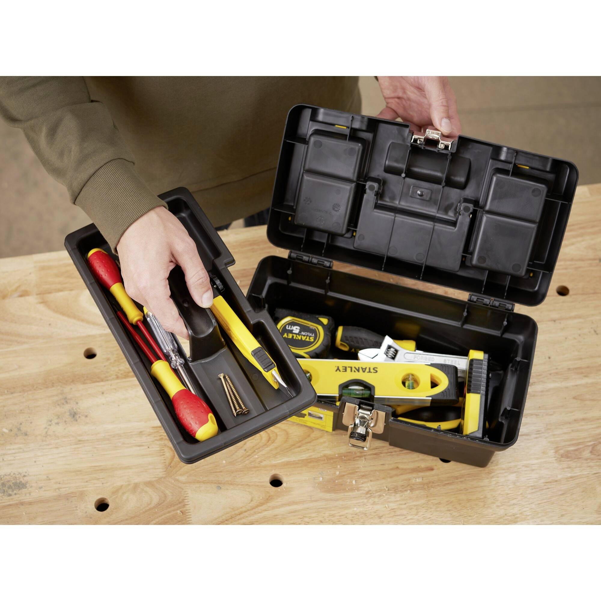 Osoba otwiera skrzynkę z narzędziami na stole. Różne narzędzia, takie jak śrubokręty i miara zwijana, są widoczne.