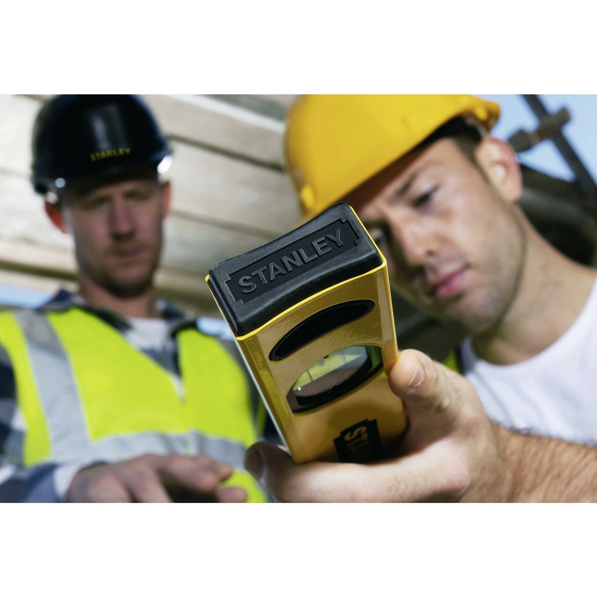 Dwóch robotników budowlanych w kaskach ochronnych i kamizelkach używa laserowego dalmierza na placu budowy, aby wykonać precyzyjne pomiary.