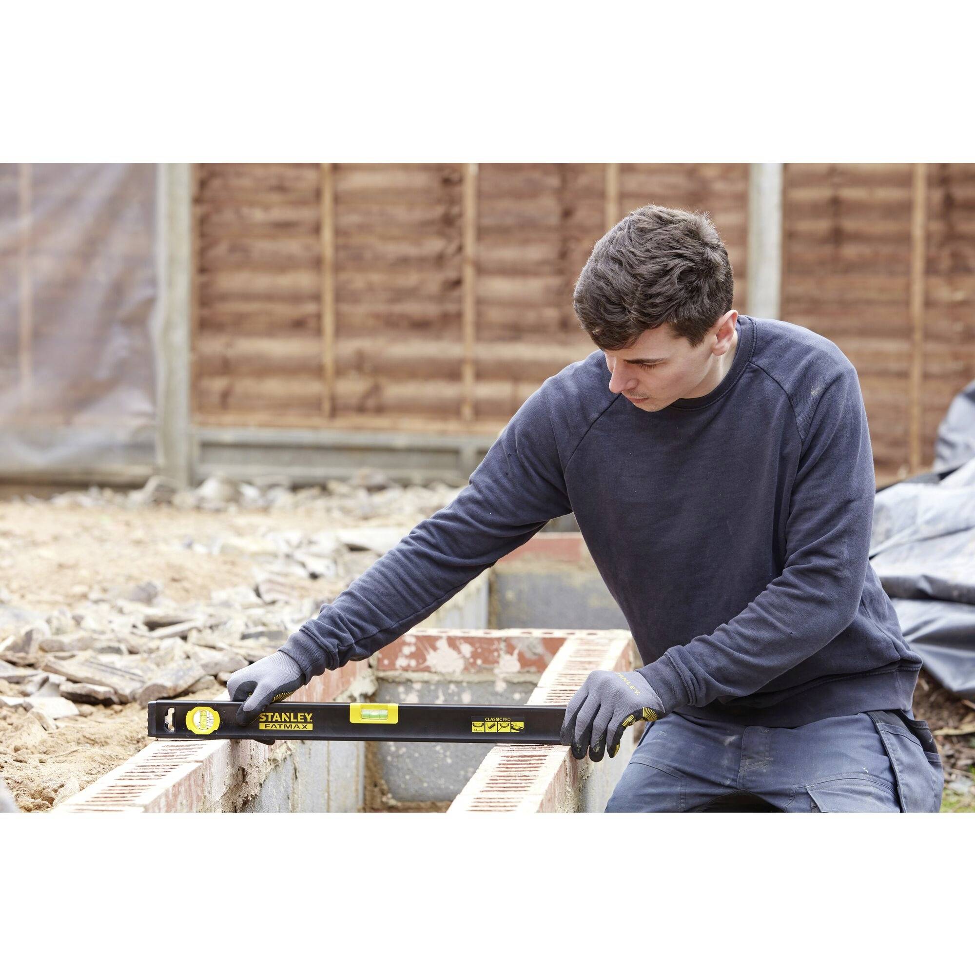 Robotnik budowlany używa poziomicy, aby sprawdzić wyrównanie cegieł na placu budowy.