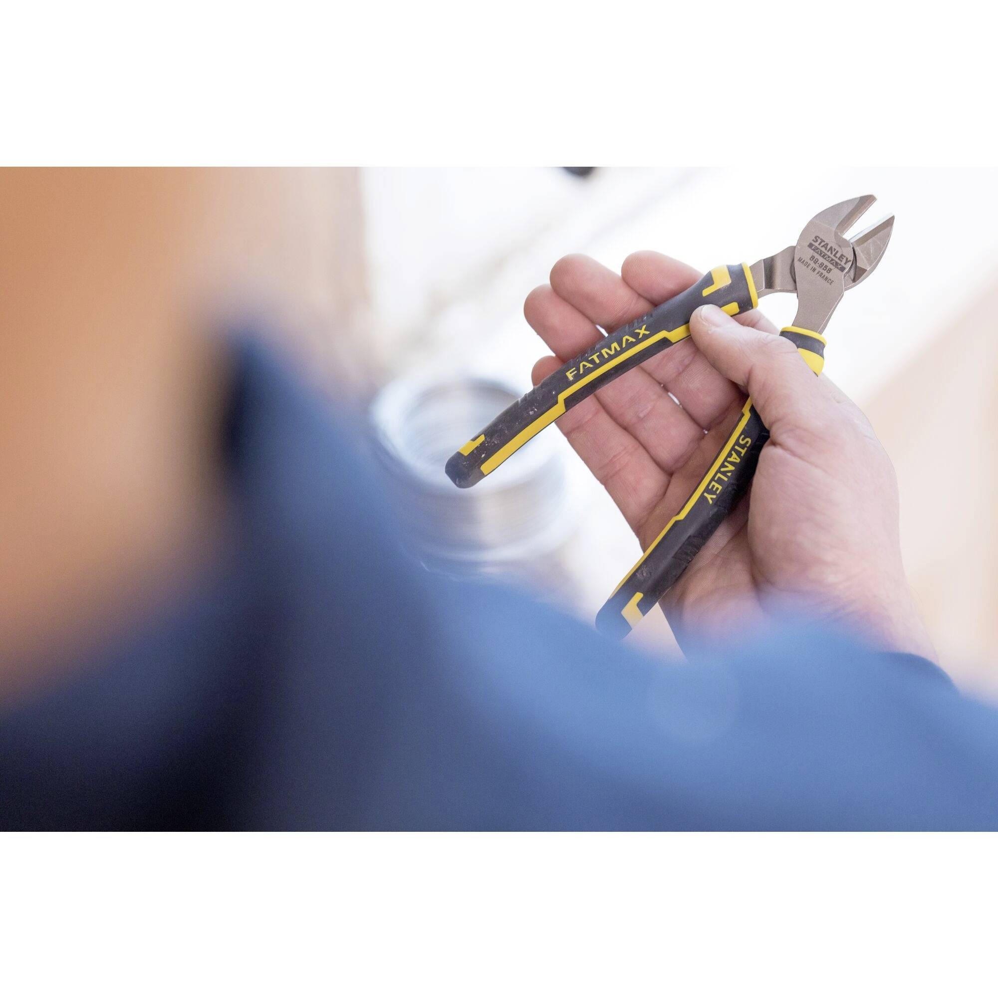 Osoba trzyma obcinacz boczny firmy Knipex w ręku, gotowa do przecięcia czegoś. W tle niewyraźnie widać rurę.