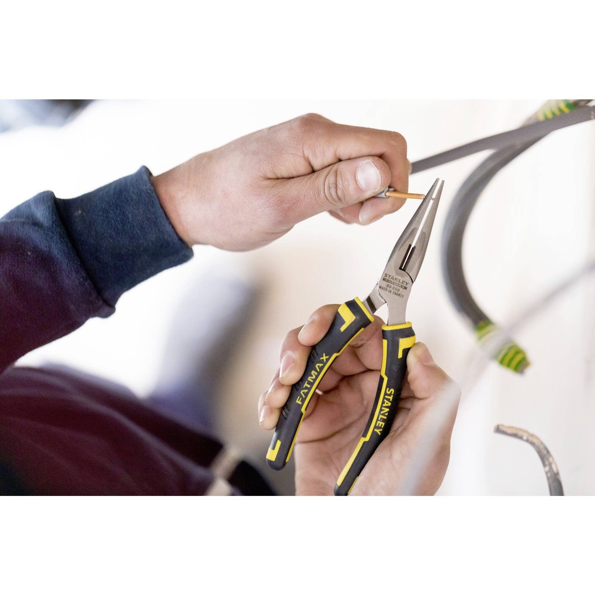 'Ręce trzymają szczypce do cięcia przewodów. Jedna osoba używa narzędzia z żółtą rękojeścią do precyzyjnych prac elektroinstalacyjnych.'