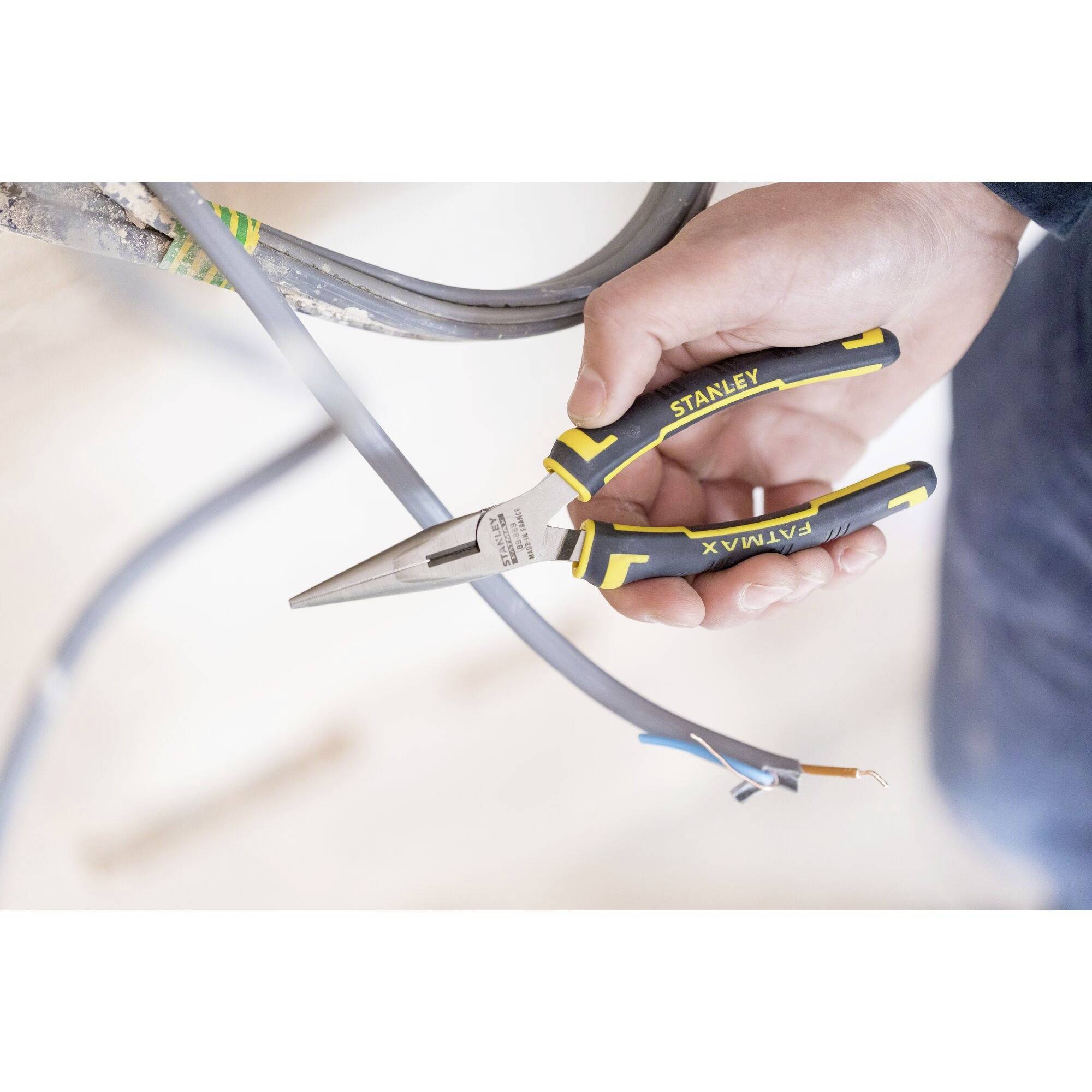 Dłoń trzyma kombinerki, które przecinają przewód elektryczny. Narzędzie posiada uchwyty w kolorach żółto-czarnych i jest używane do cięcia kabli.