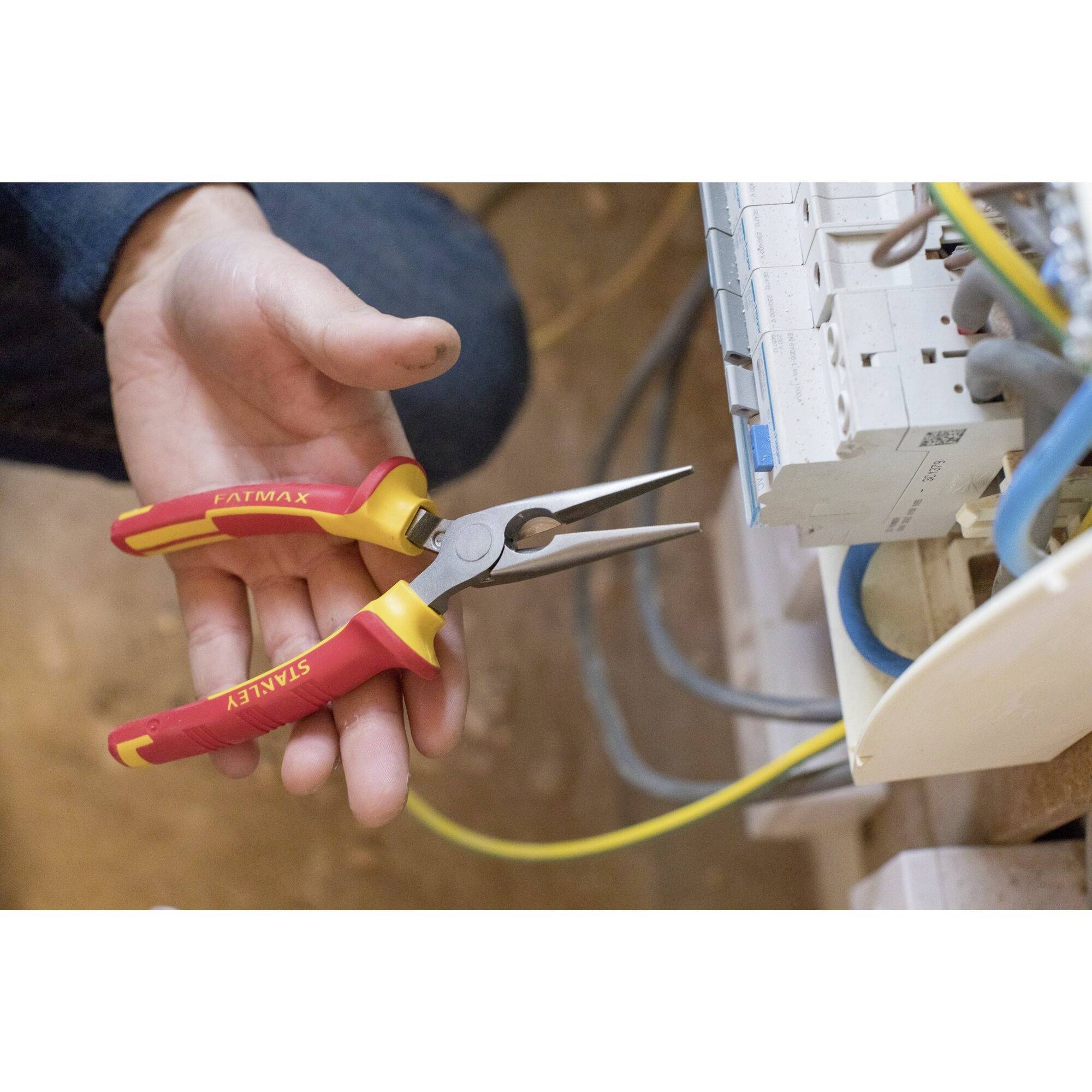 Osoba trzyma długie szczypce precyzyjne i pracuje przy tablicy rozdzielczej z wieloma kablami.