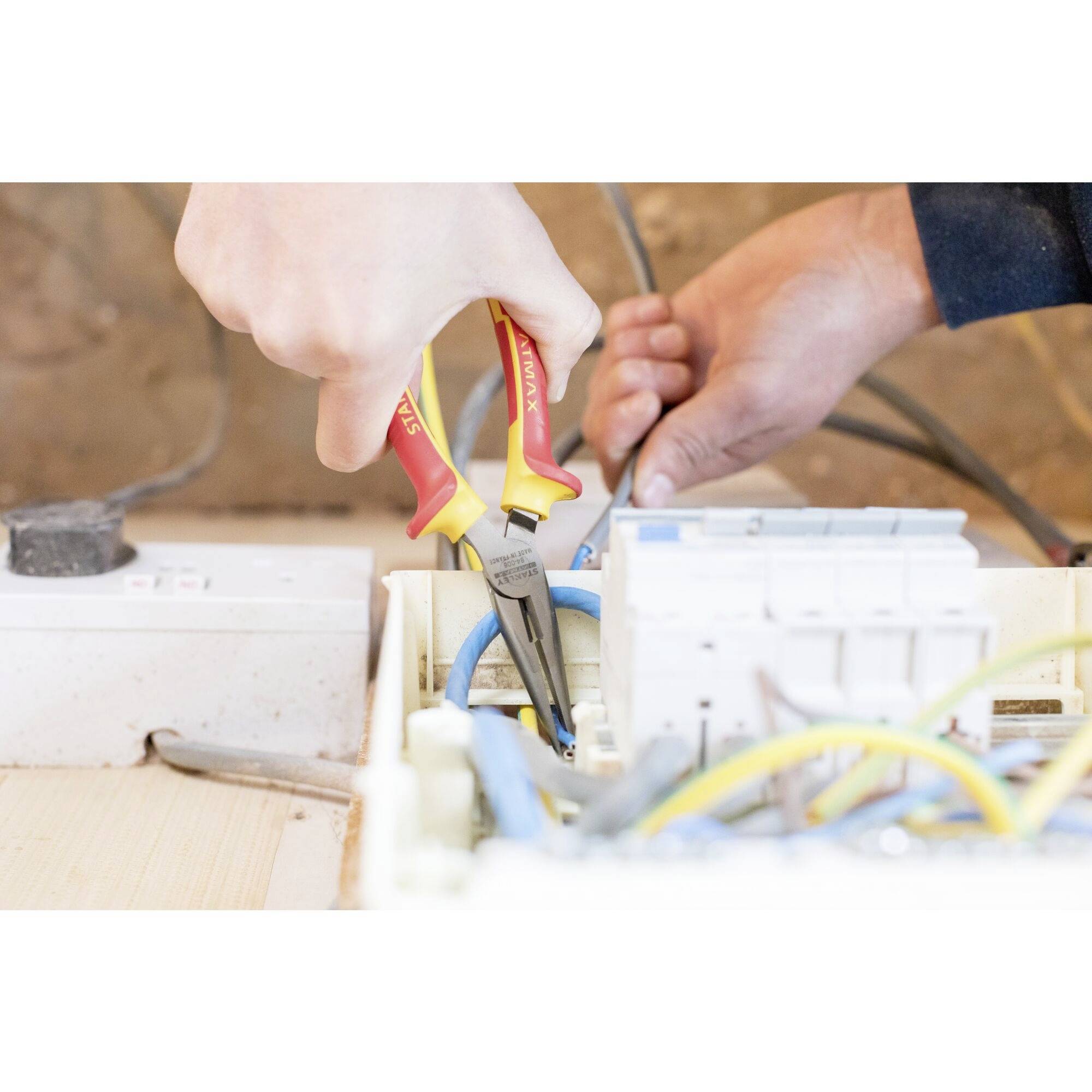 Osoba używa izolowanych szczypiec podczas pracy przy skrzynce elektrycznej. Widoczne są rękawice ochronne.