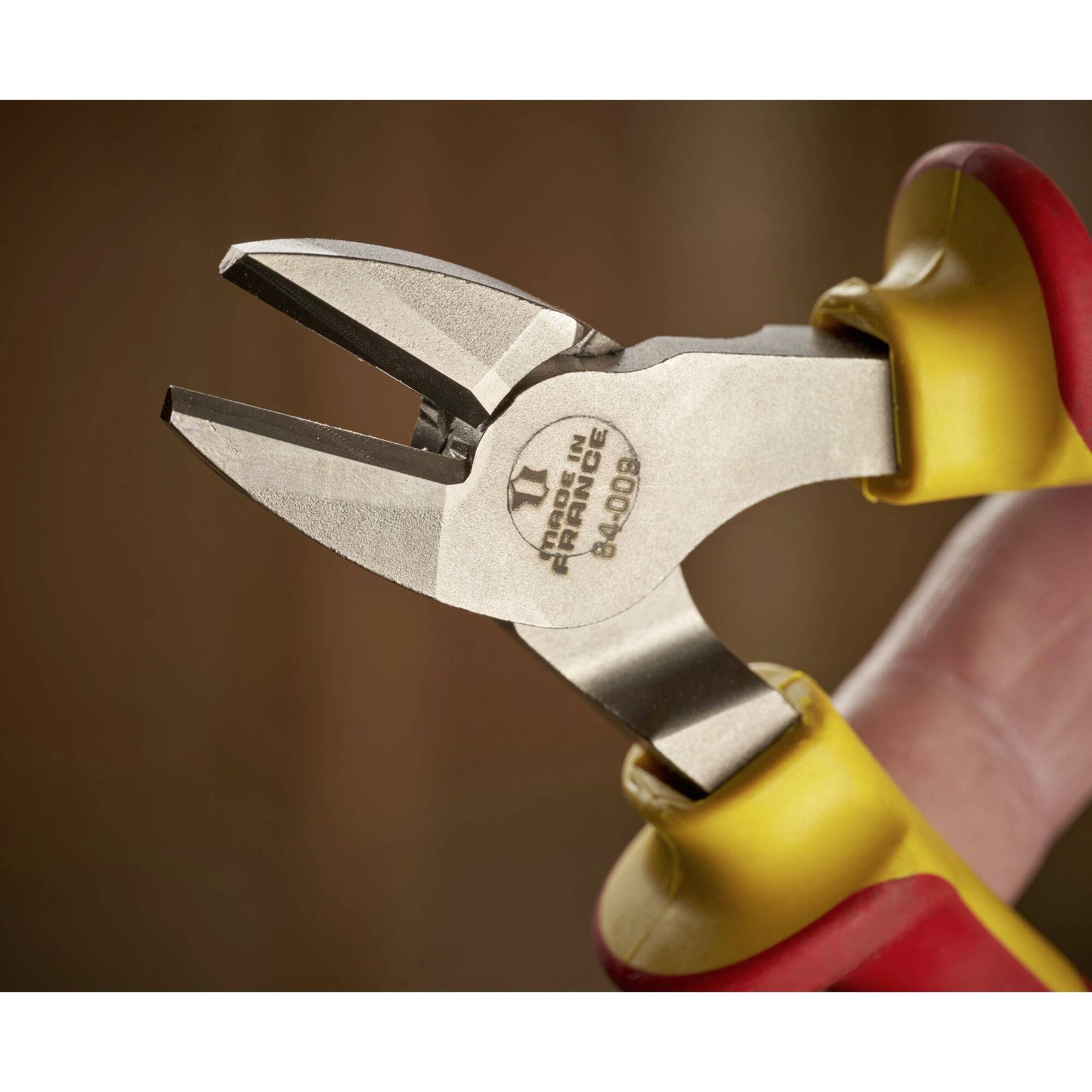 Żółto-czerwone szczypce z rozchylonymi szczękami, przeznaczone do cięcia drutu. Leżą na niewyraźnym tle.