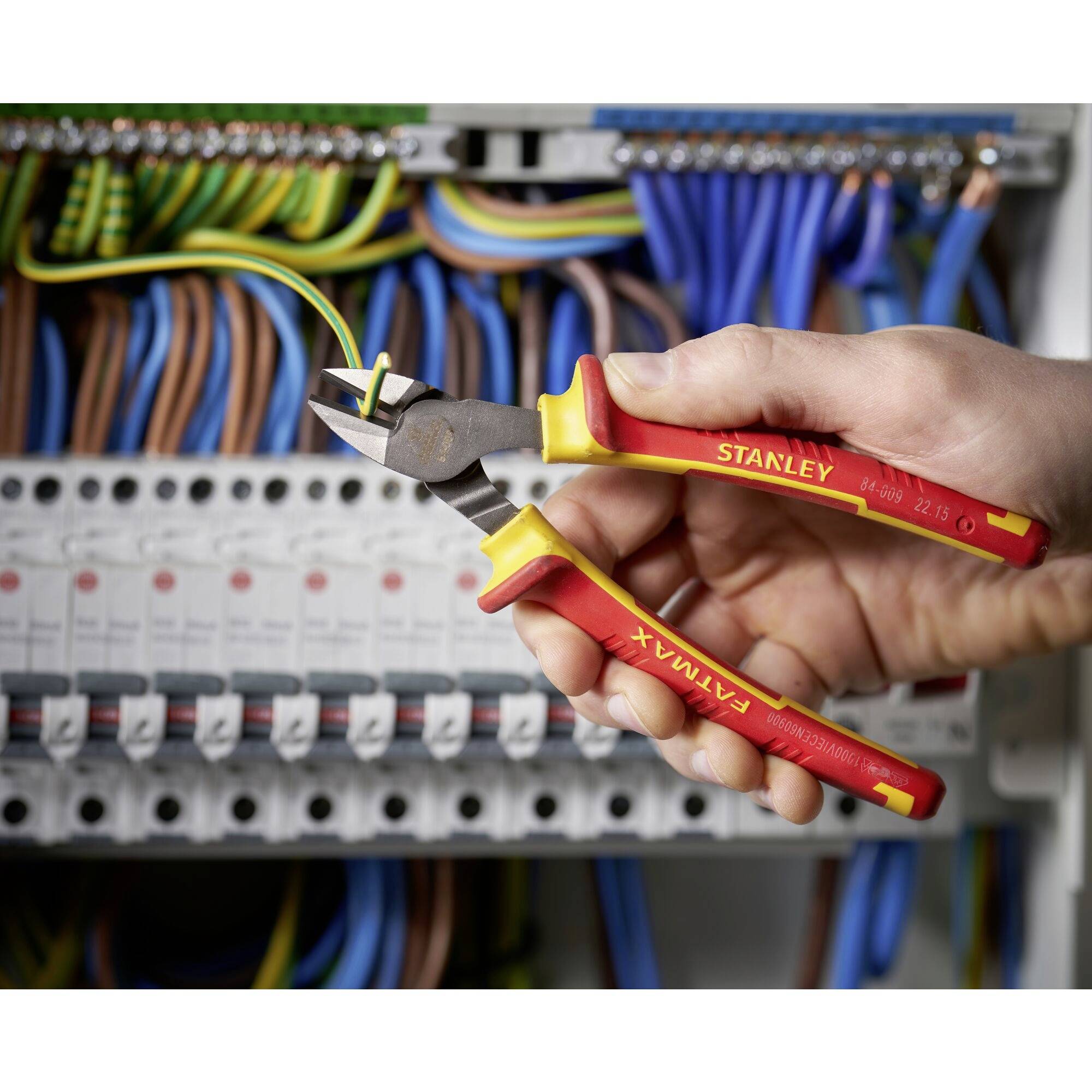 Ręka trzyma obcinacz boczny i przecina kabel przed tablicą rozdzielczą z kolorowymi przewodami.