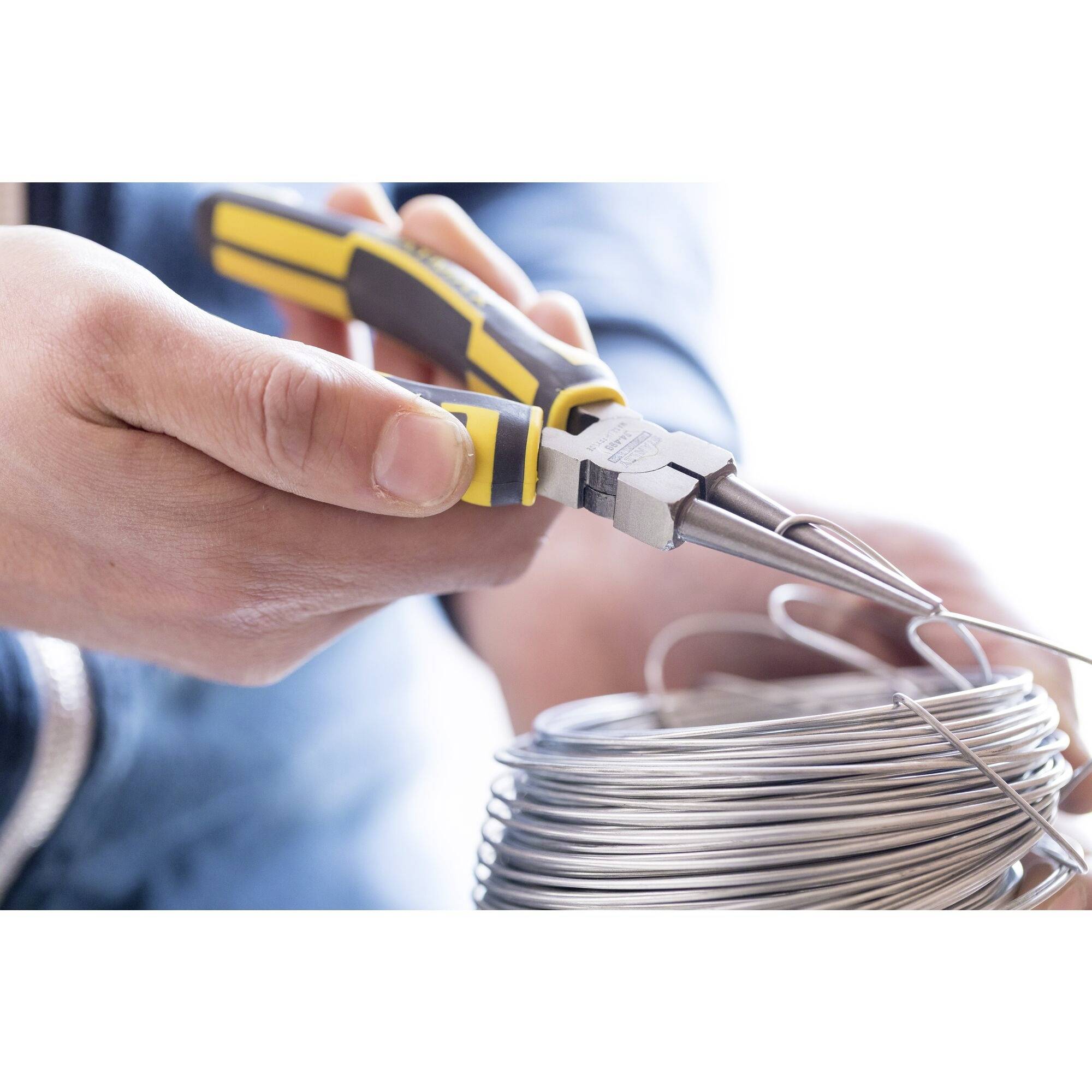 Osoba trzyma szczypce i zgina kawałek drutu z rolki drutu. W tle rozmycie.