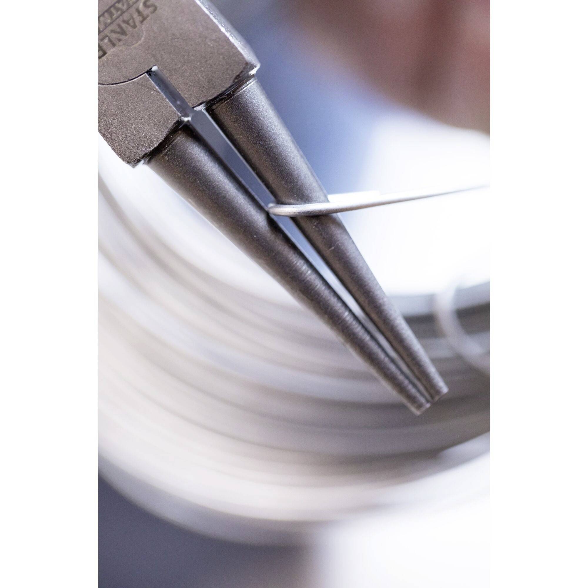 Zbliżenie szczypiec do cięcia drutu, które zaginają przewód. W tle rozmyte metaliczne powierzchnie.