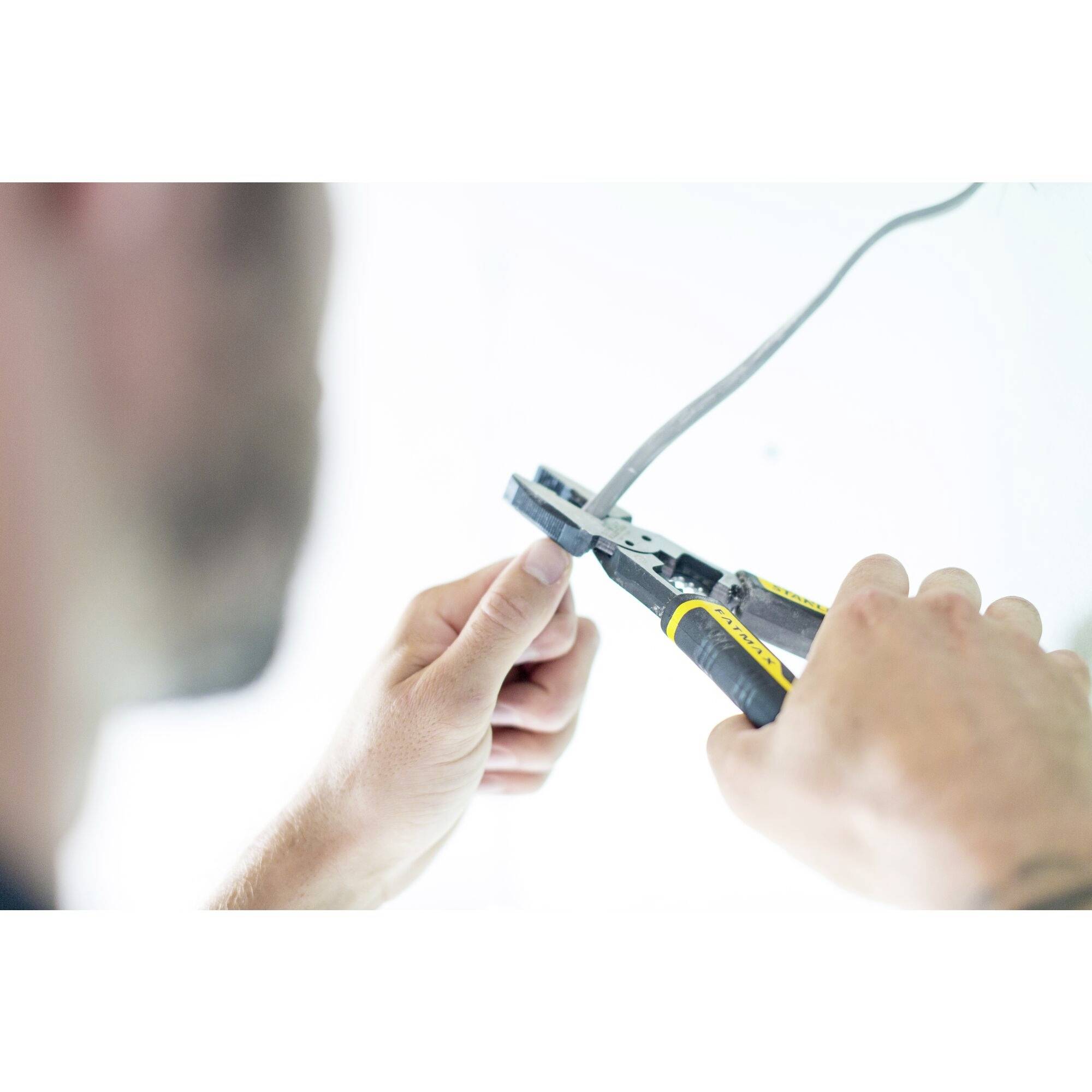 Osoba używa szczypiec do ściągania izolacji, aby odsłonić koniec przewodu. Scena przedstawia rzemieślniczy proces pracy.