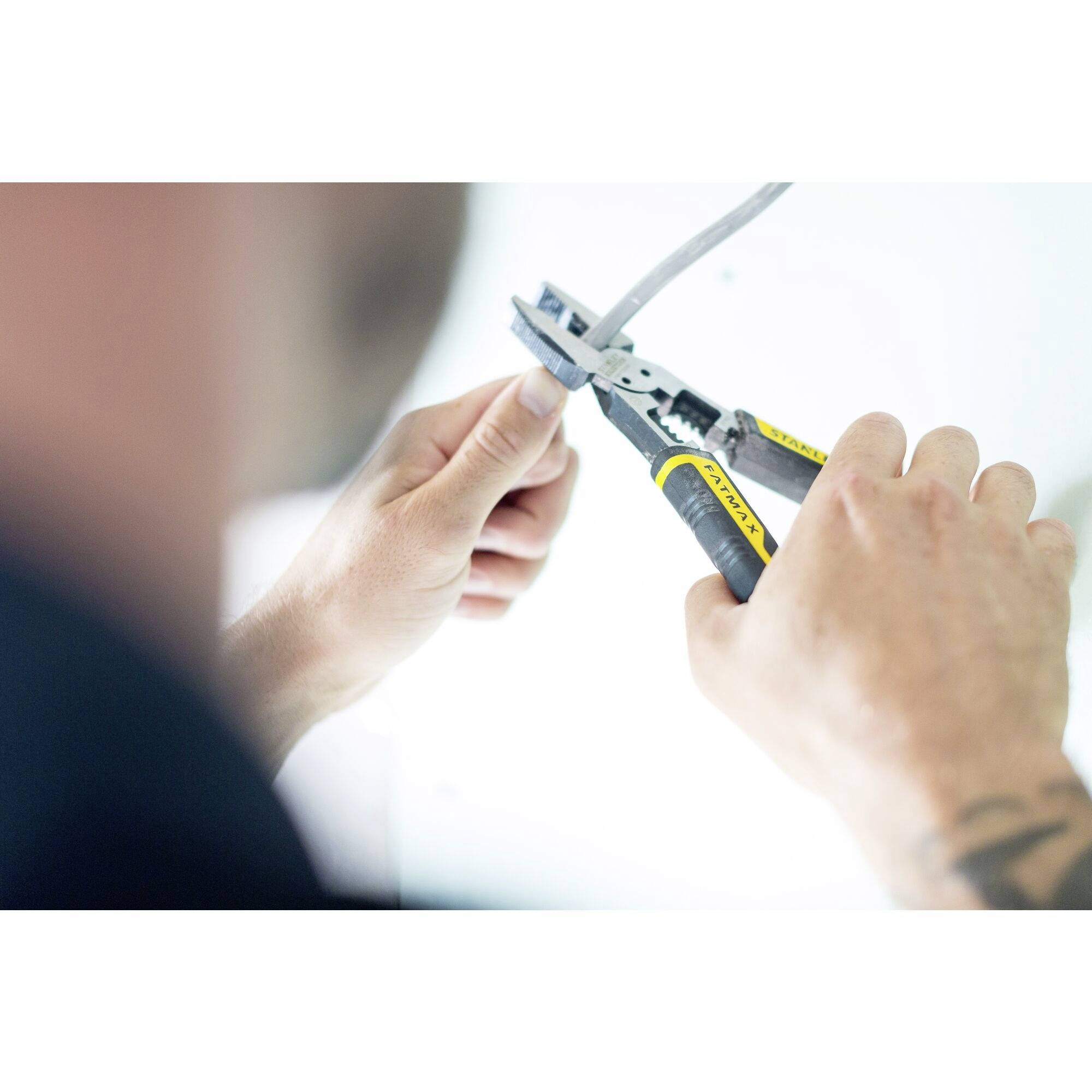 Osoba ściąga izolację z przewodu szczypczykami. Fokus jest na rękach i narzędziu.