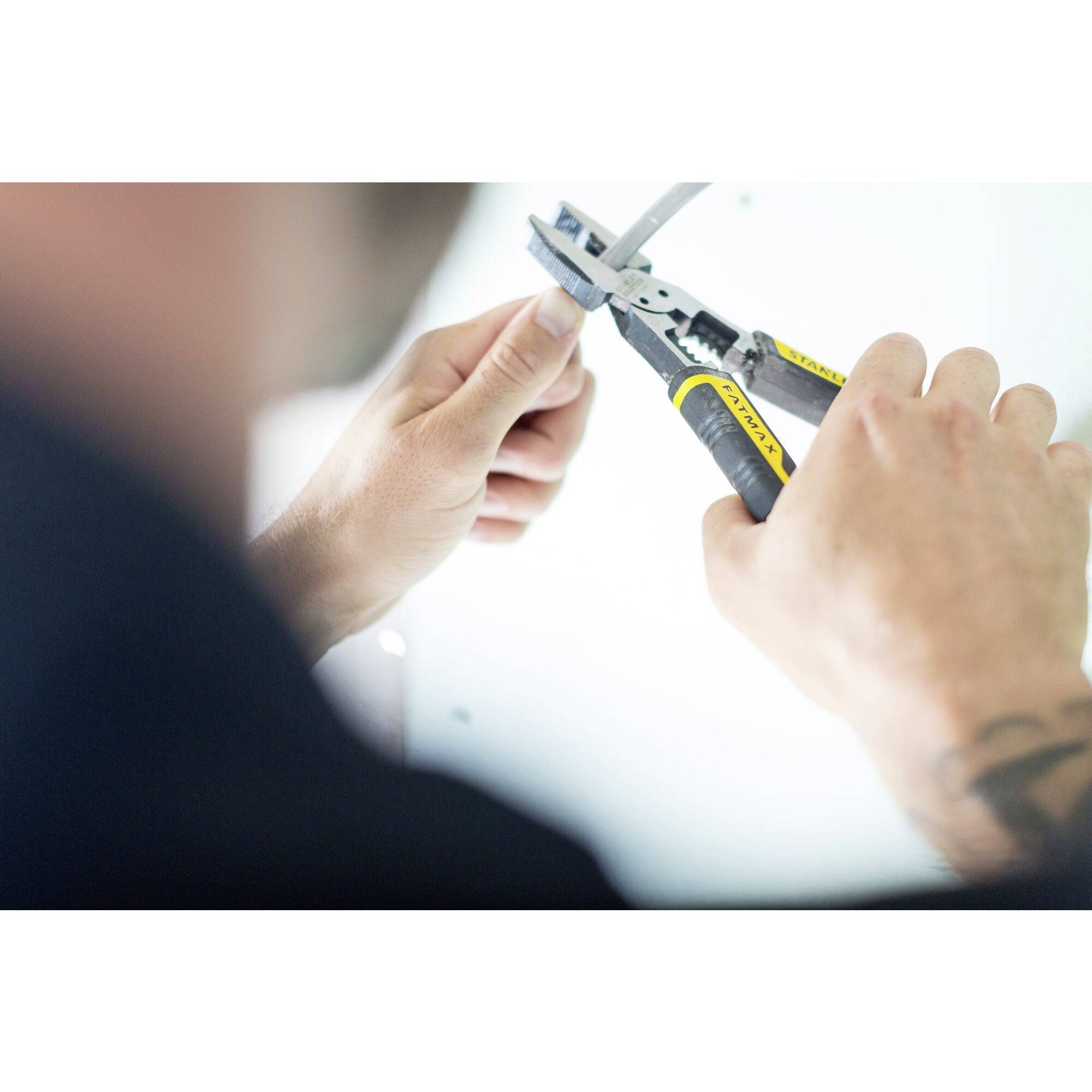 Osoba pracuje przy kablu, trzymając go jedną ręką i używając szczypiec w drugiej ręce.